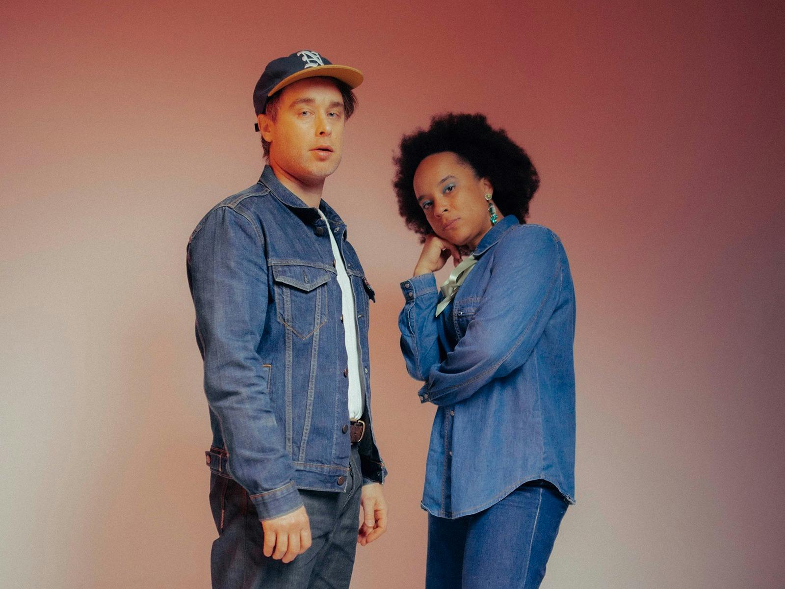 Two artists against a red backdrop wearing double denim