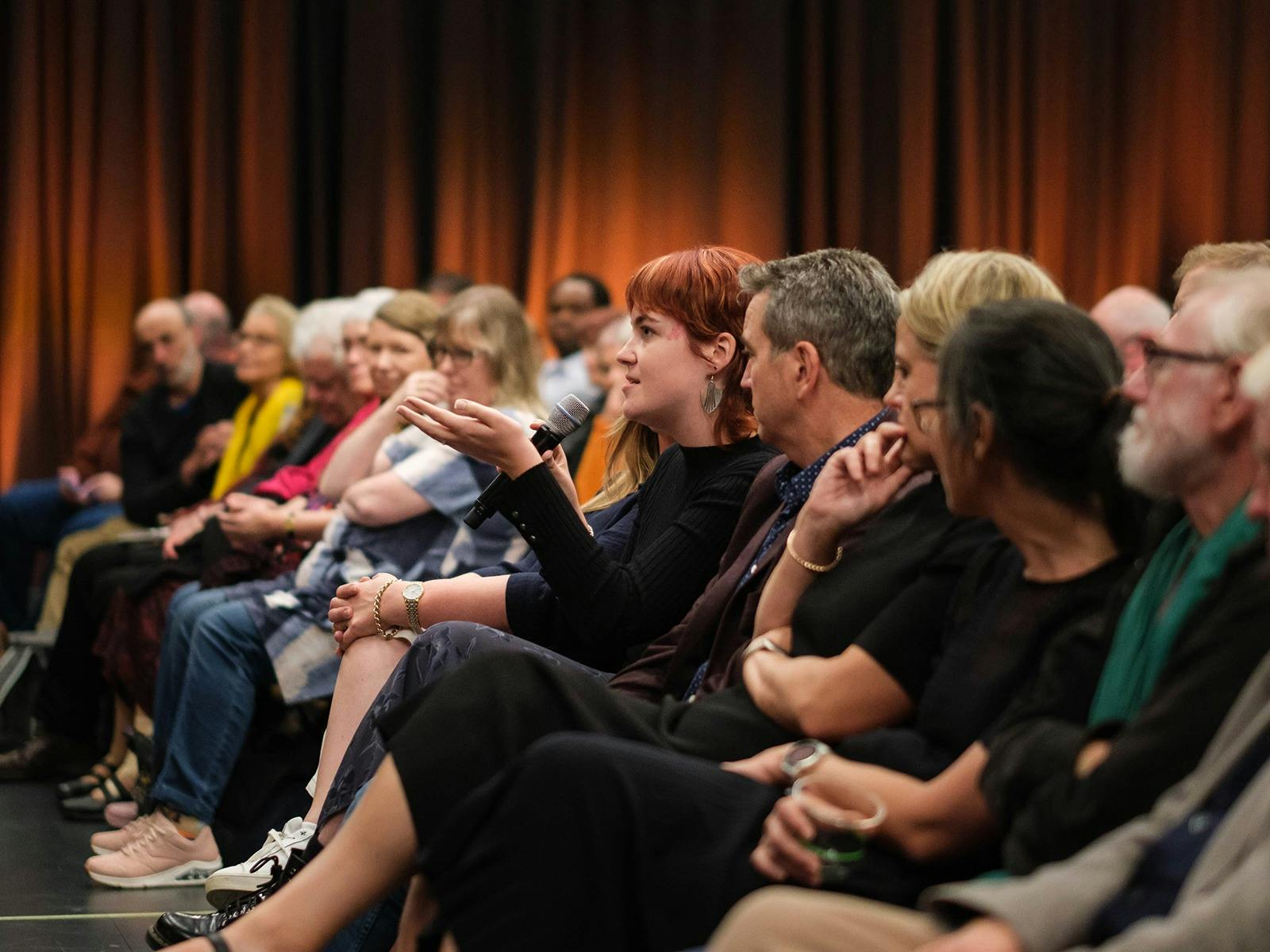 A person is sitting in an audience holding a microphone