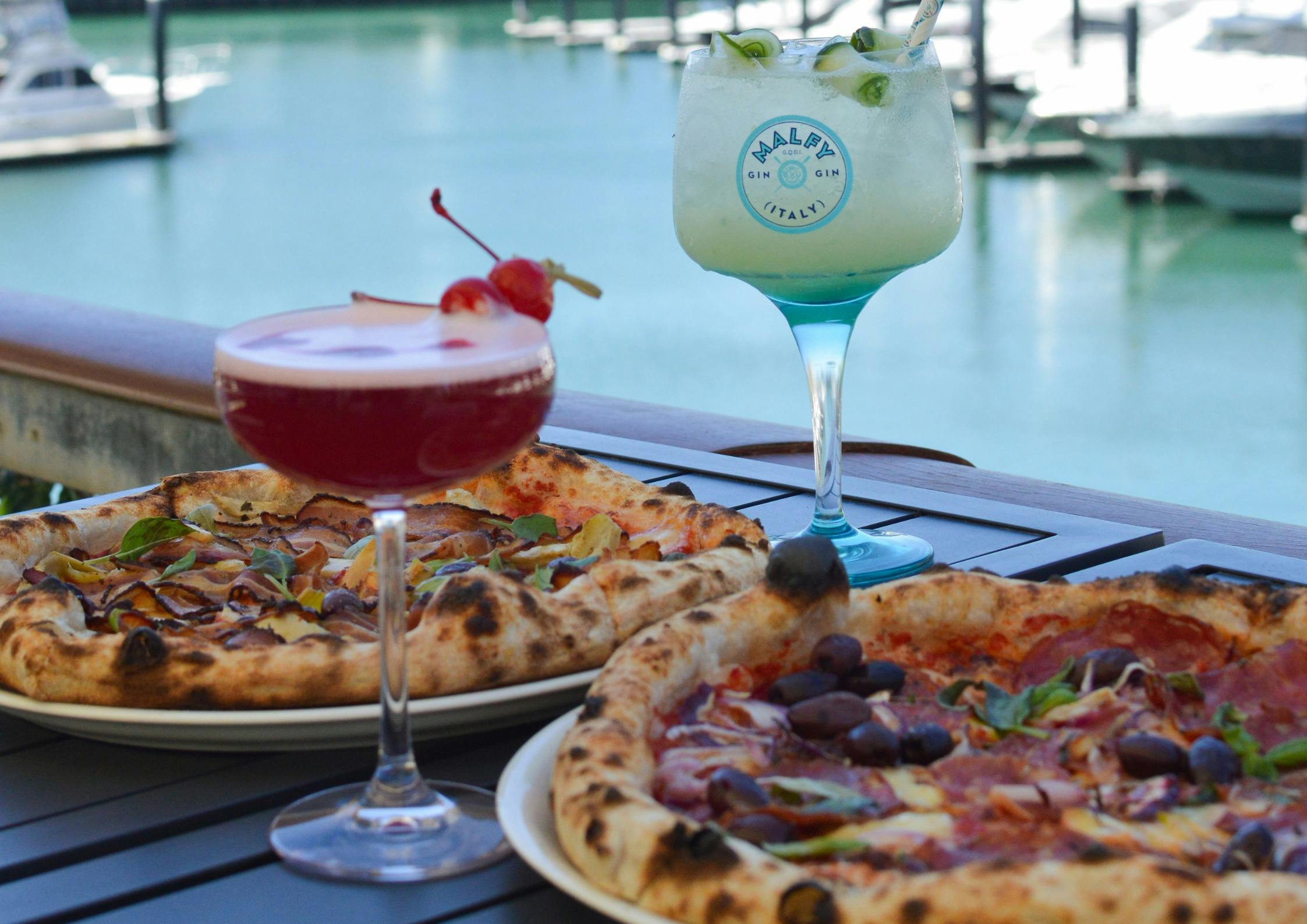 two cocktails and two pizzas by the water marina pier