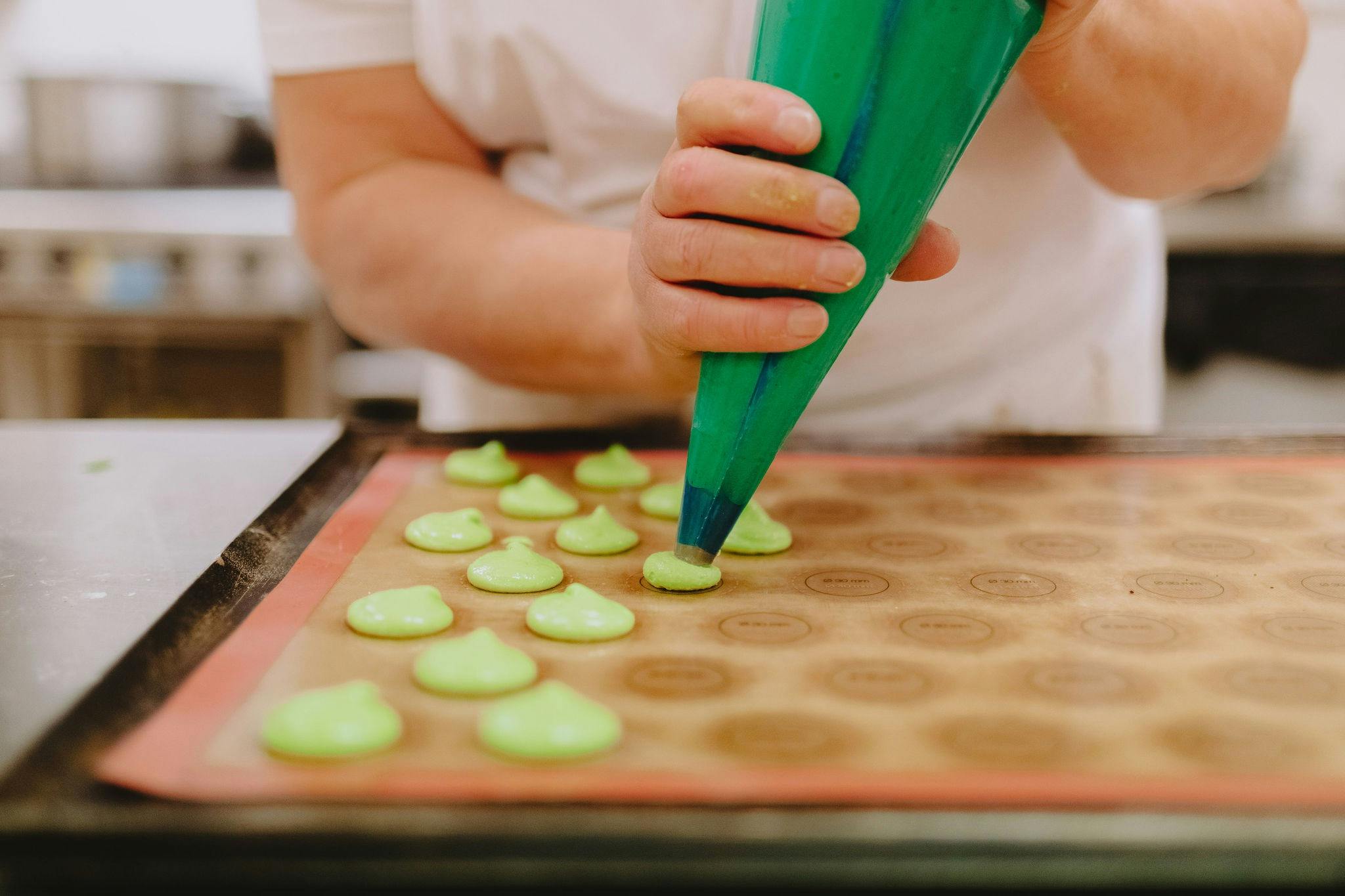 A baker piping green coloured macaroons with precision onto the baking tray.