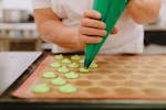 A baker piping green coloured macaroons with precision onto the baking tray.