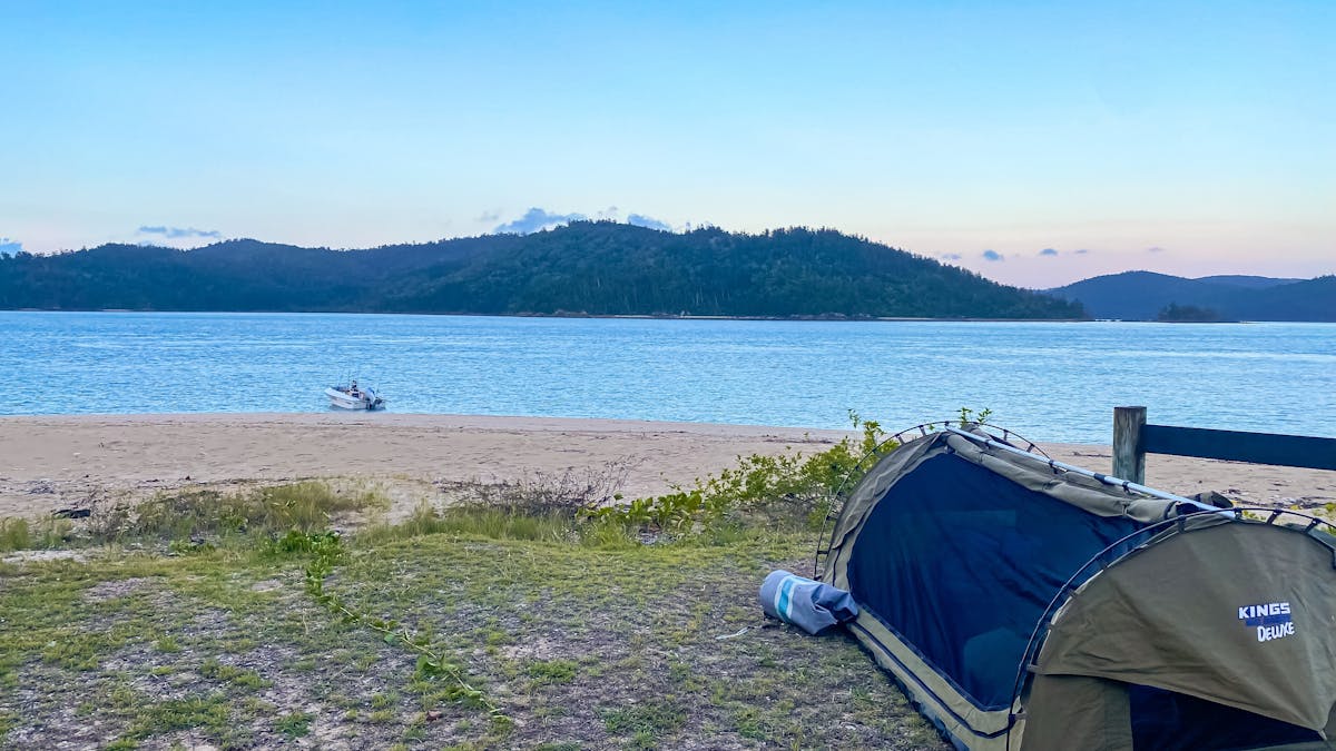 Swag tent on Henning Island grassy edge of beach and small boat in water close to beach