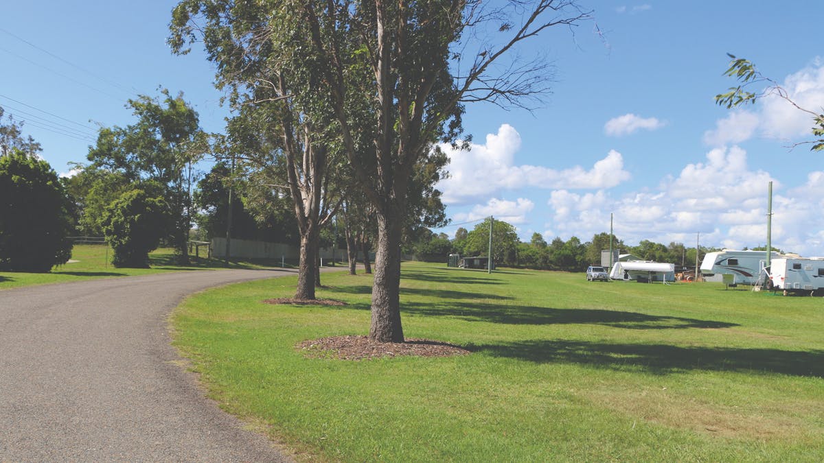 Kilcoy Showgrounds - part of the road with green grass, gumtrees and caravans in the distance.