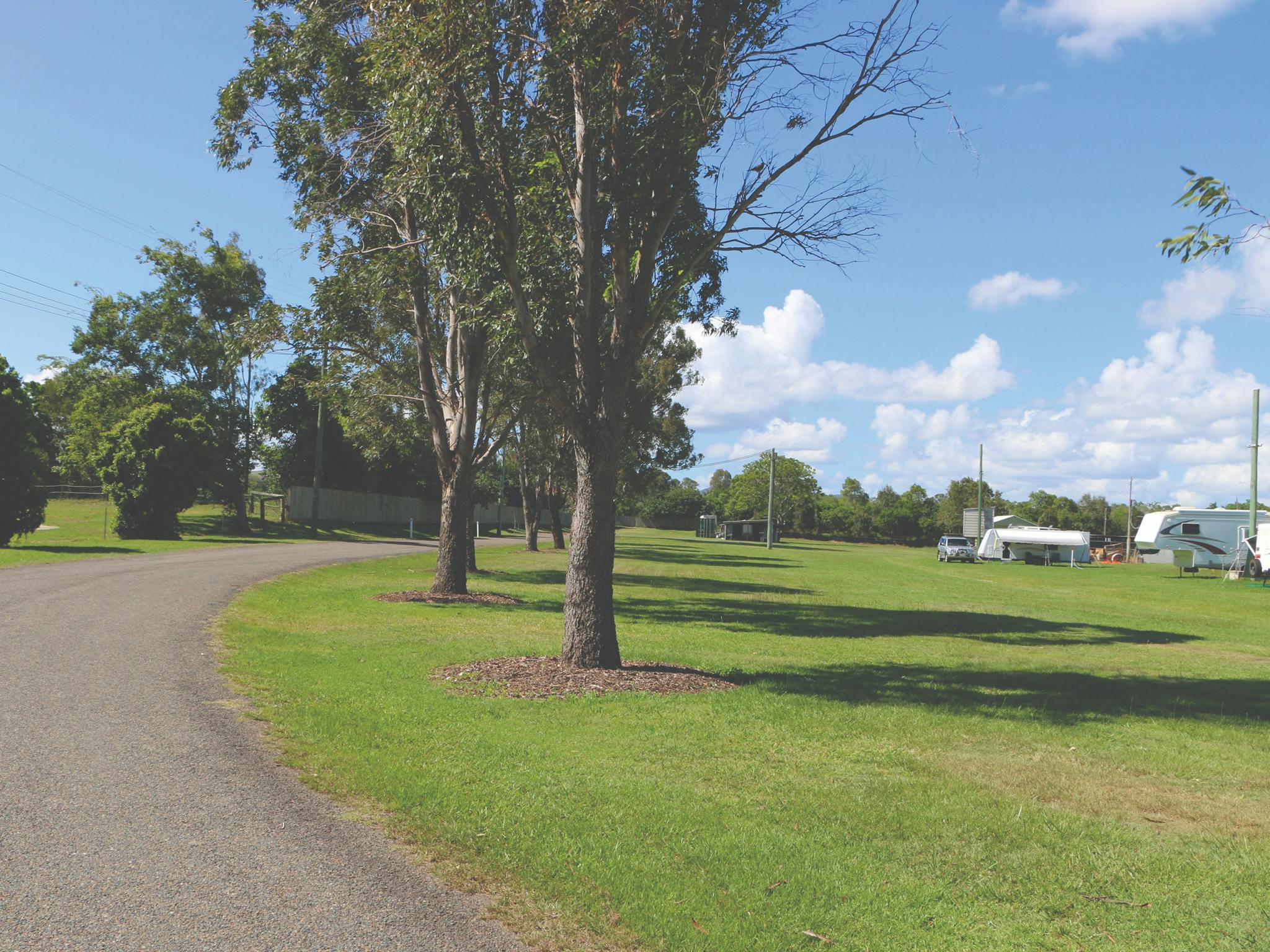 Kilcoy Showgrounds - part of the road with green grass, gumtrees and caravans in the distance. Kilcoy Showgrounds - part of the road with green grass, gumtrees and caravans in the distance.