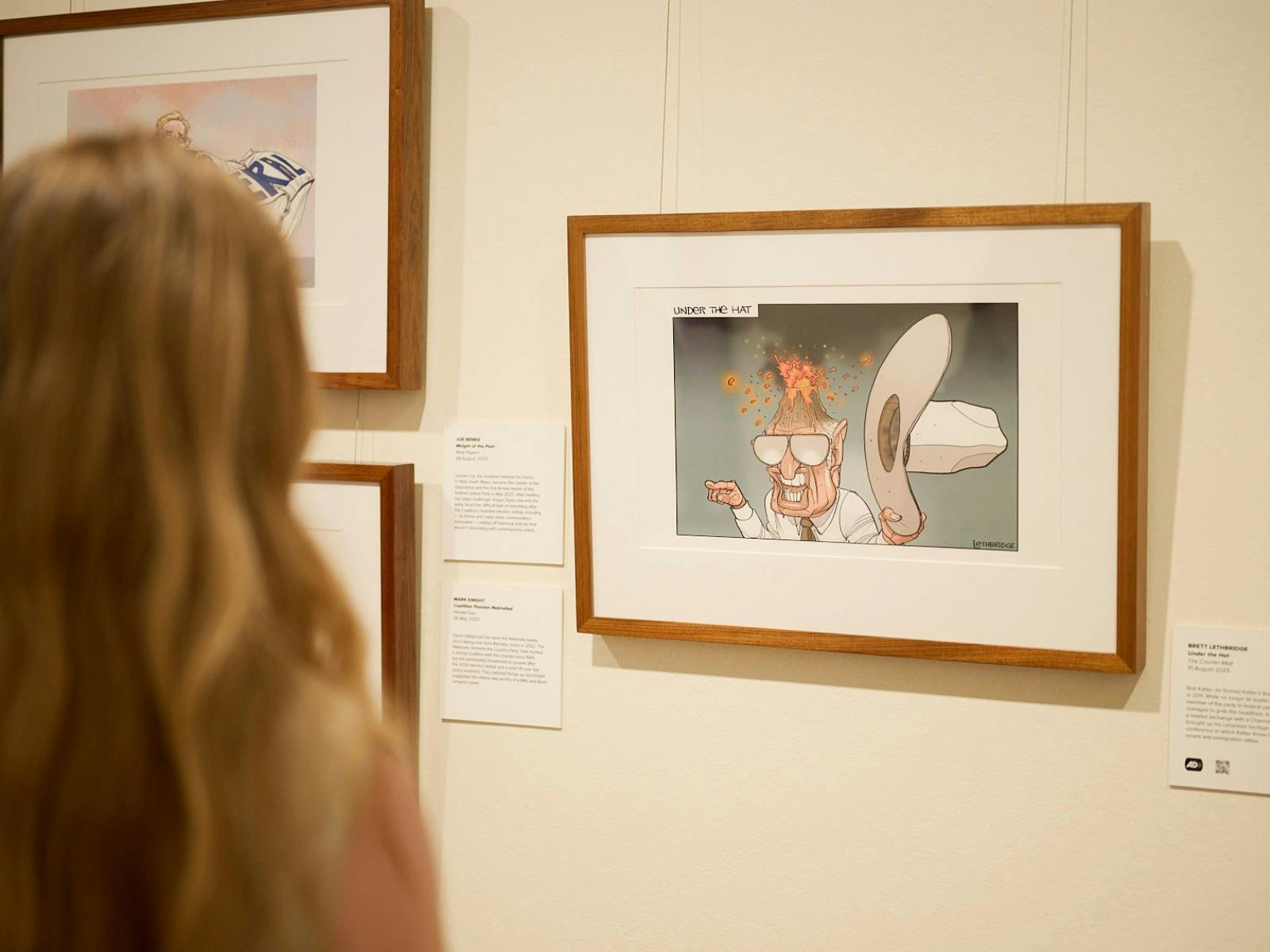Woman views framer political cartoon in gallery.