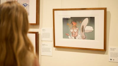Woman views framer political cartoon in gallery.