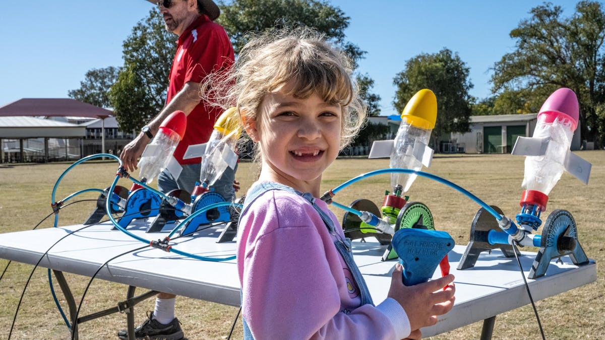 A small girl in a pink shirt in front of  colourful bottle rockets