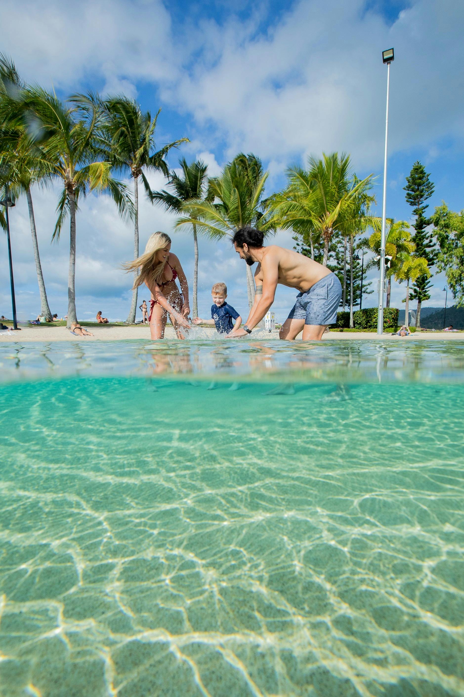 Couple and small child playing in the shallow waters of the lagoon with palm trees in the background