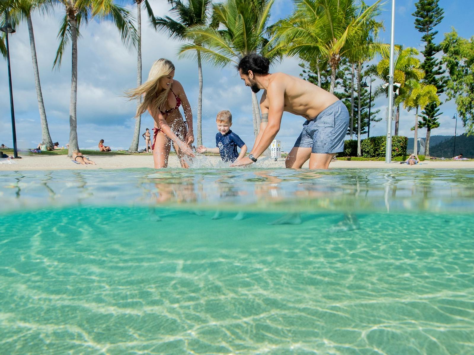 Couple and small child playing in the shallow waters of the lagoon with palm trees in the background