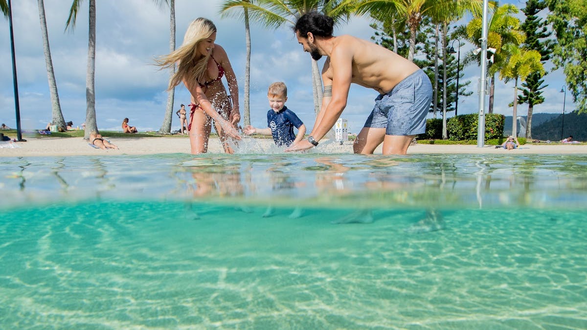 Couple and small child playing in the shallow waters of the lagoon with palm trees in the background