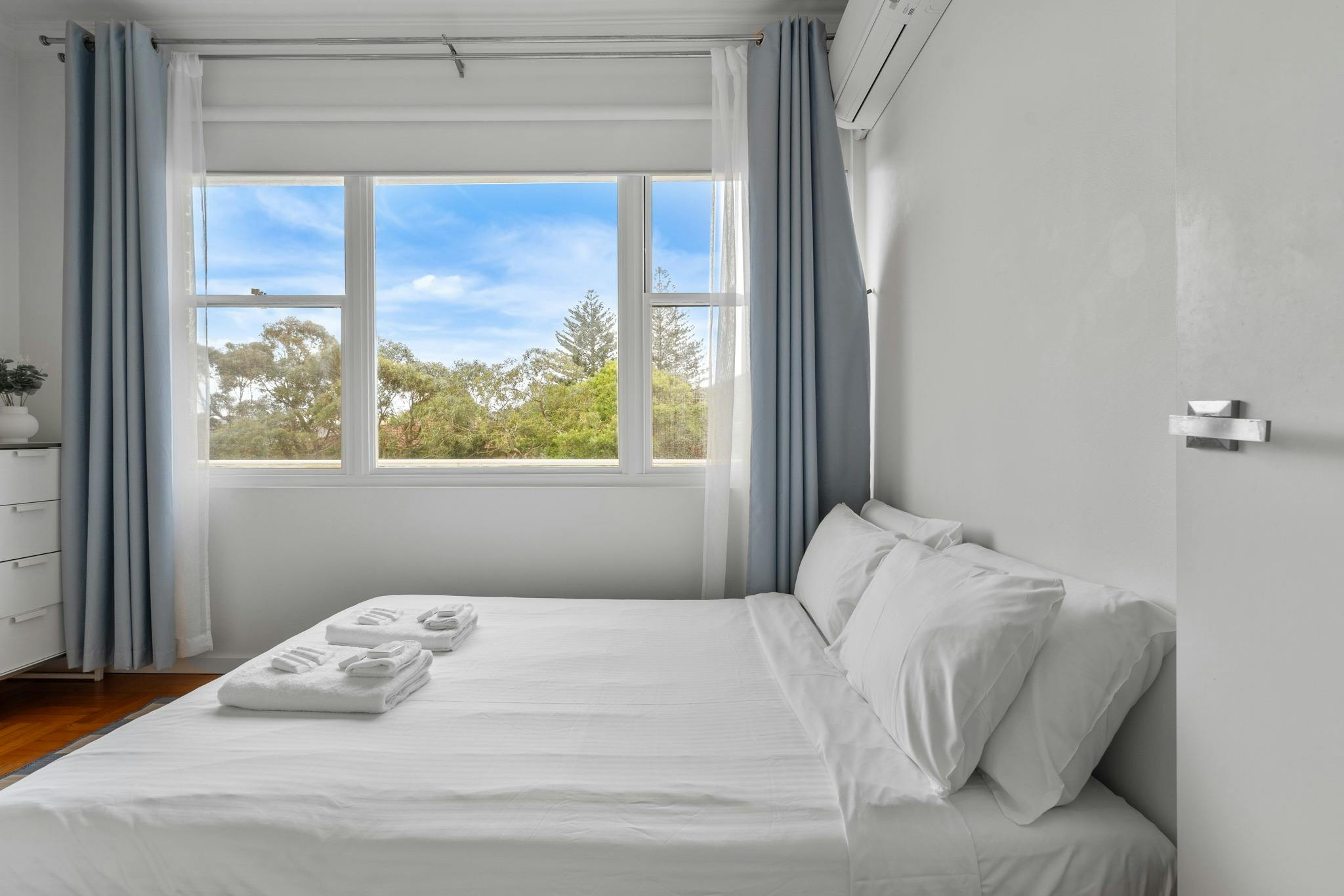 舒適的臥室配有白色床單、藍色窗簾和外面的綠色景觀。