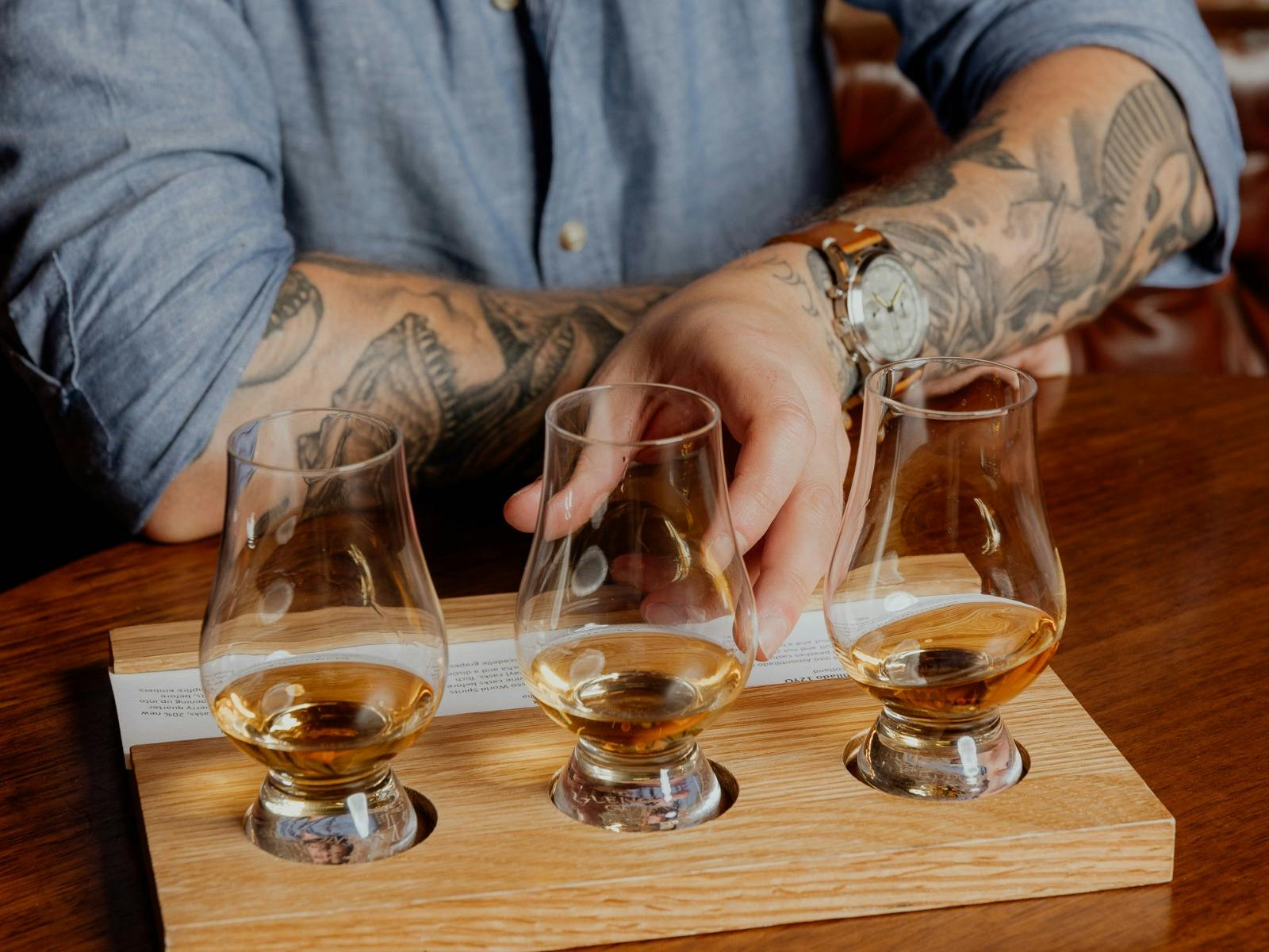 three whisky tasting glasses are placed on a wooden tasting board with whisky and tasting notes
