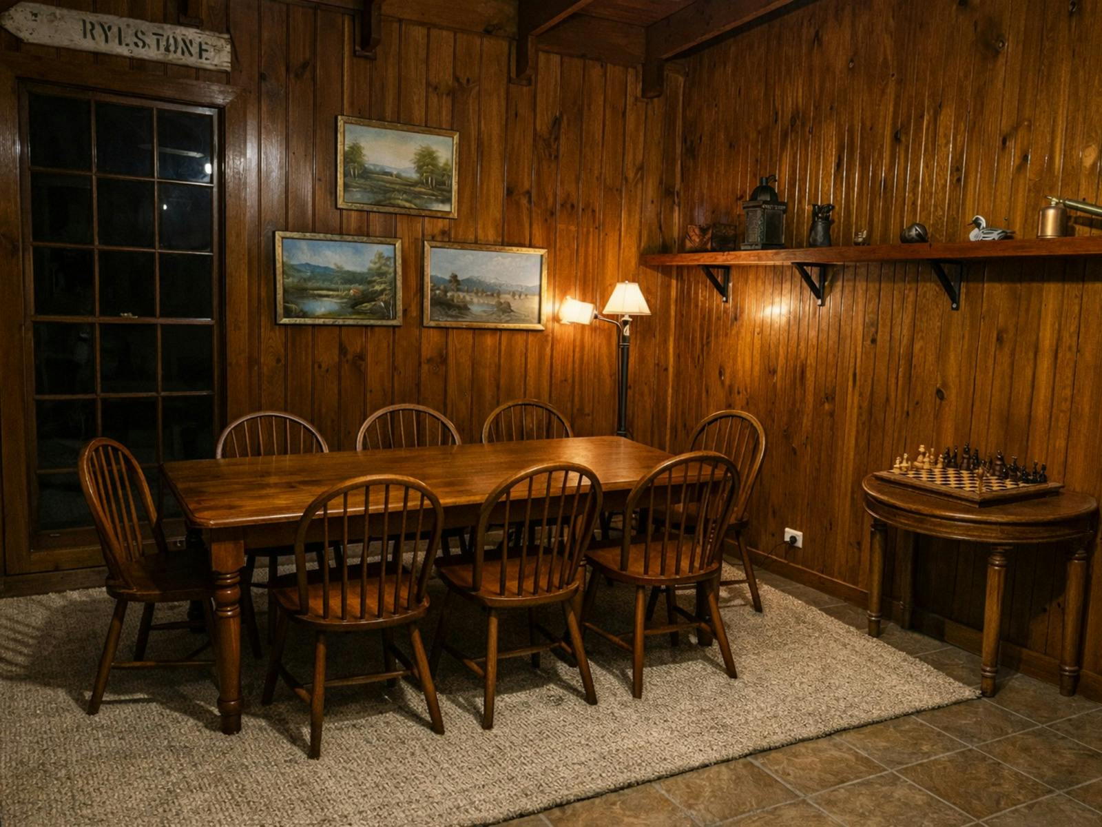 A timber-lined dining room with a long wooden table, chairs, framed artwork and a chess table
