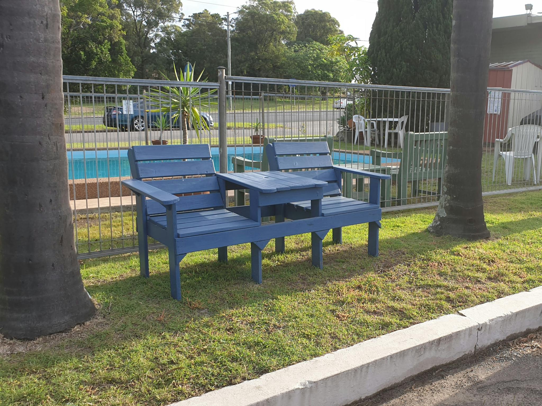 Blue Jack & Jill seat under palm trees outside pool fence
