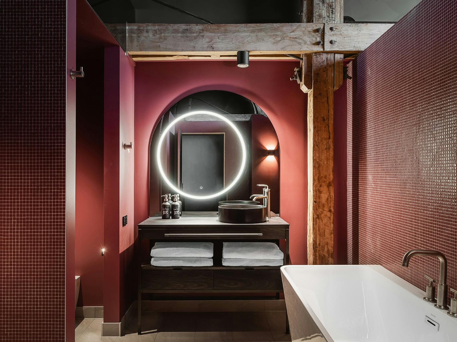 A dusty pink bathroom with vanity and back lit mirror with a bath to the side of the picture