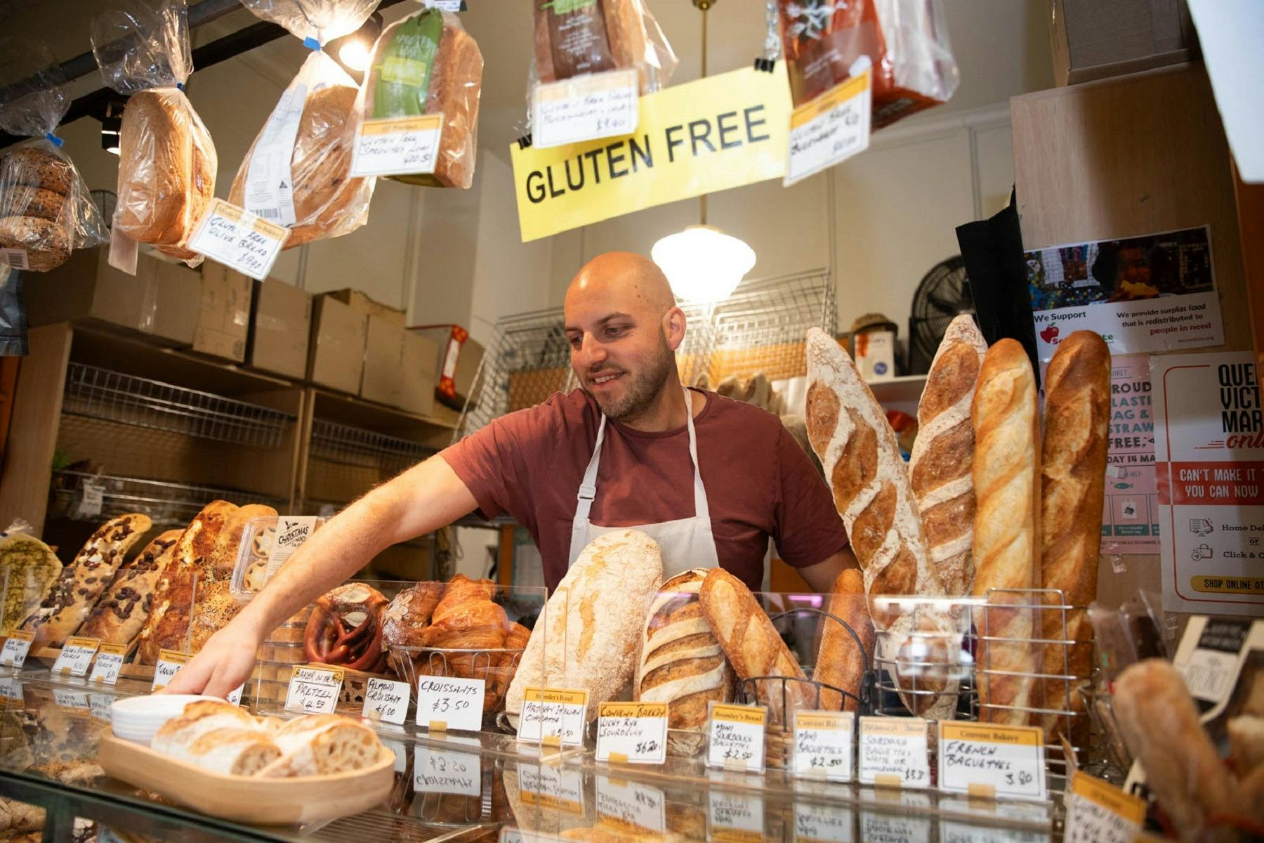 A baker standing inside a bakery with bread for sale around