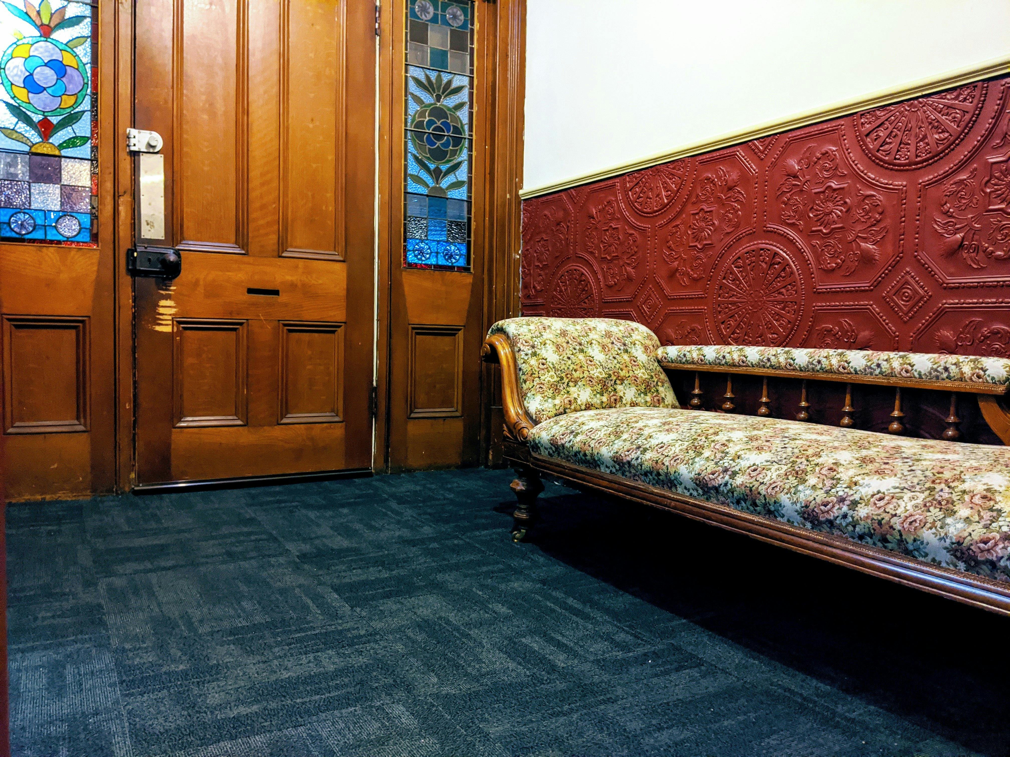 Stained glass and wood entry door, with a red pressed wall and floral chaise lounge