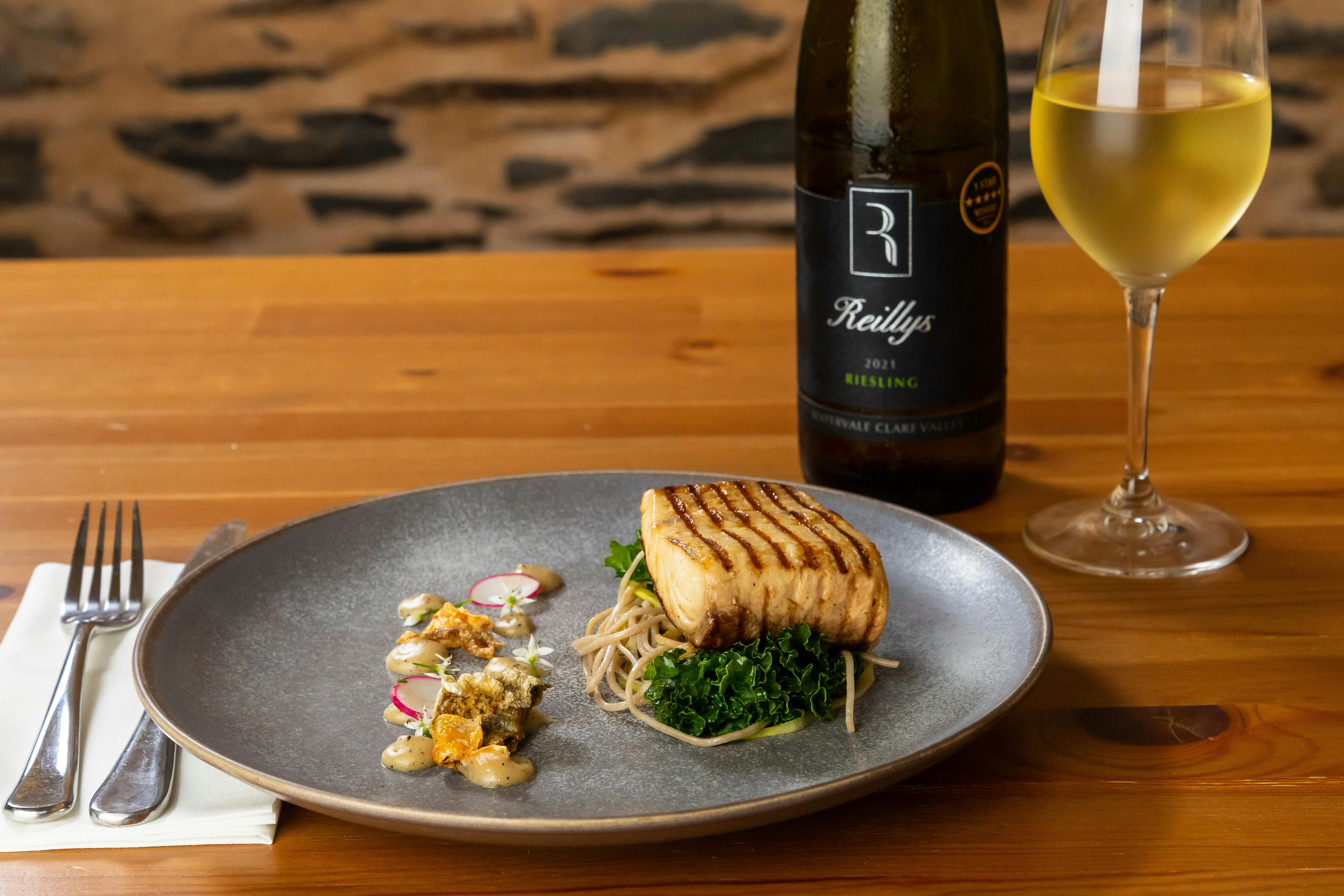 Bottle of Reillys wine and glass of yellow Riesling next to a plate of grilled fish and gourmetsalad