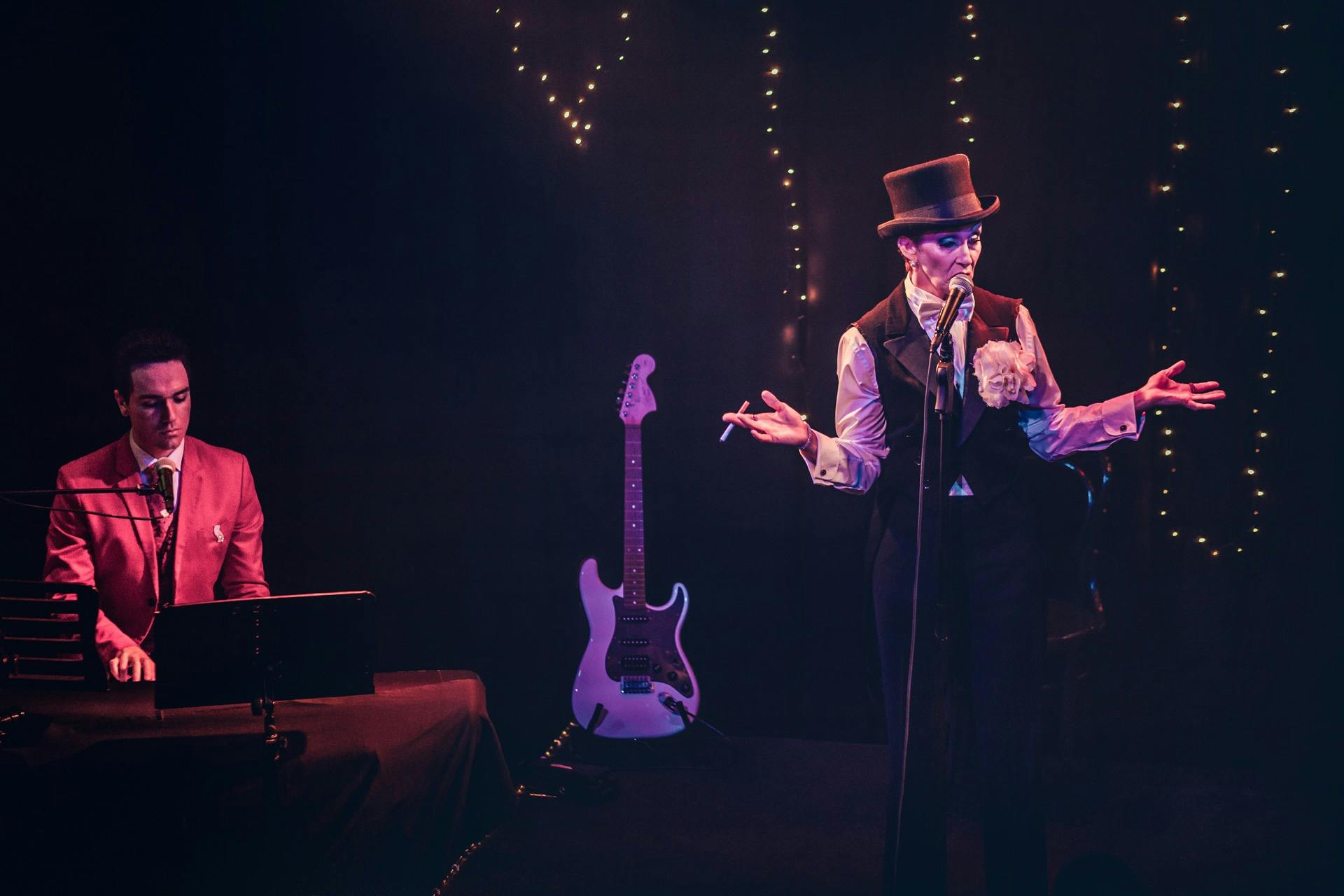 Man in red jacket playing keyboard for woman in top hat singing