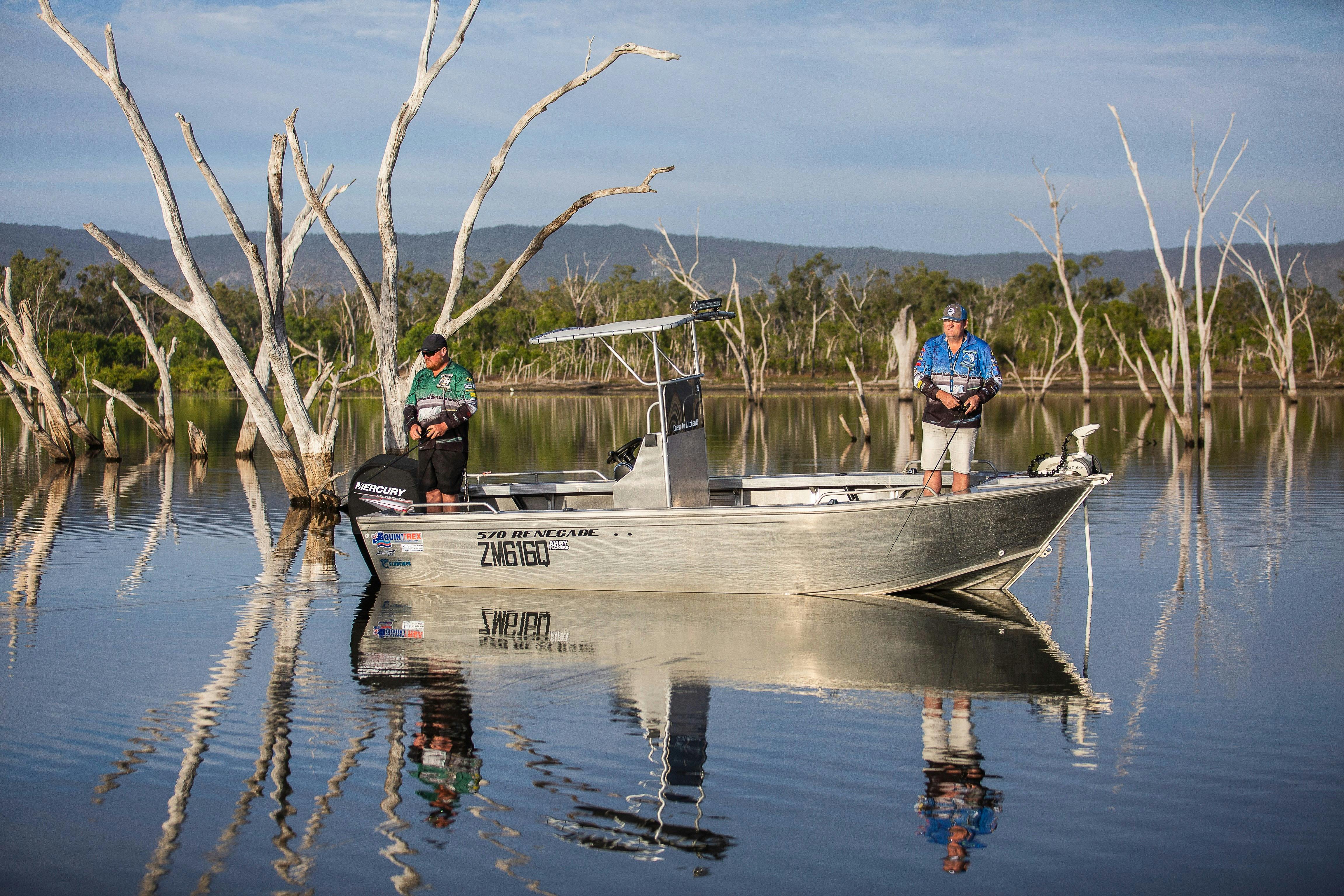 Two fisherman fishing in the calm lake waters with trees in the background