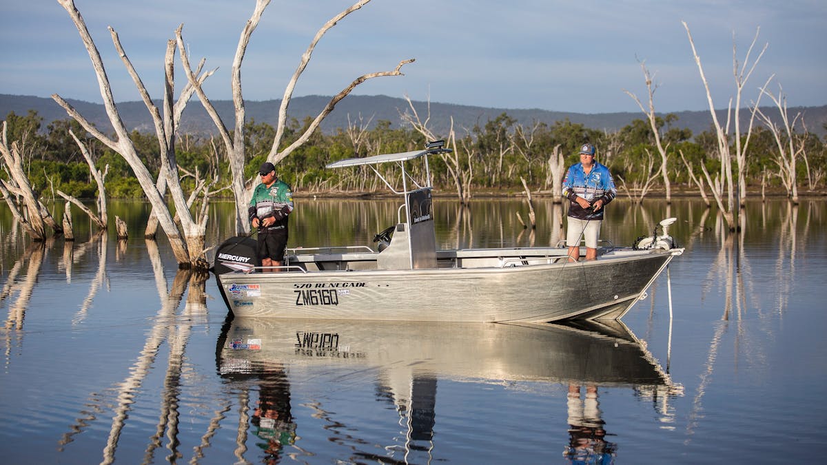 Two fisherman fishing in the calm lake waters with trees in the background