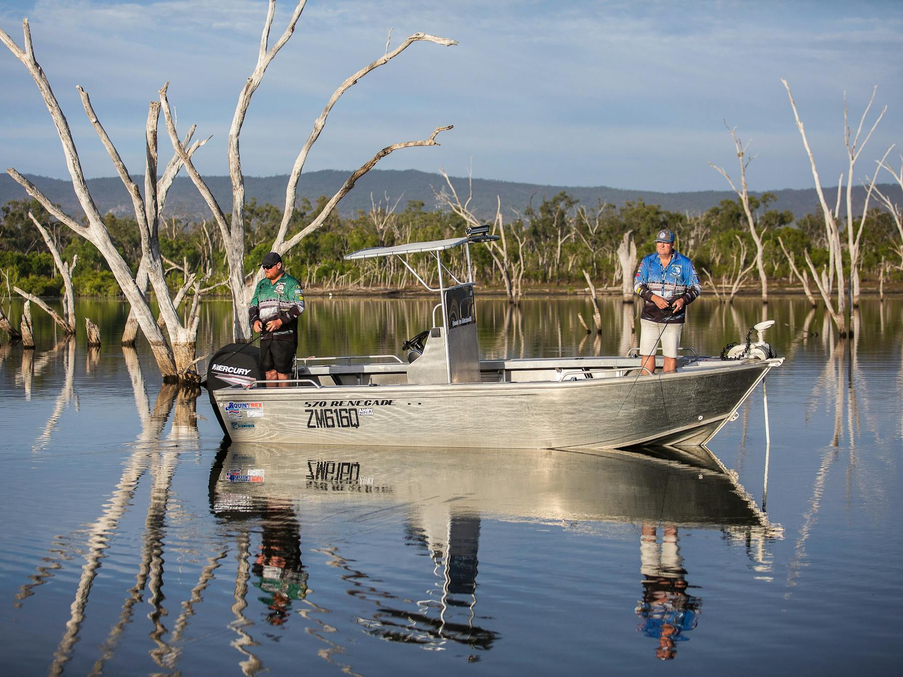 Two fisherman fishing in the calm lake waters with trees in the background