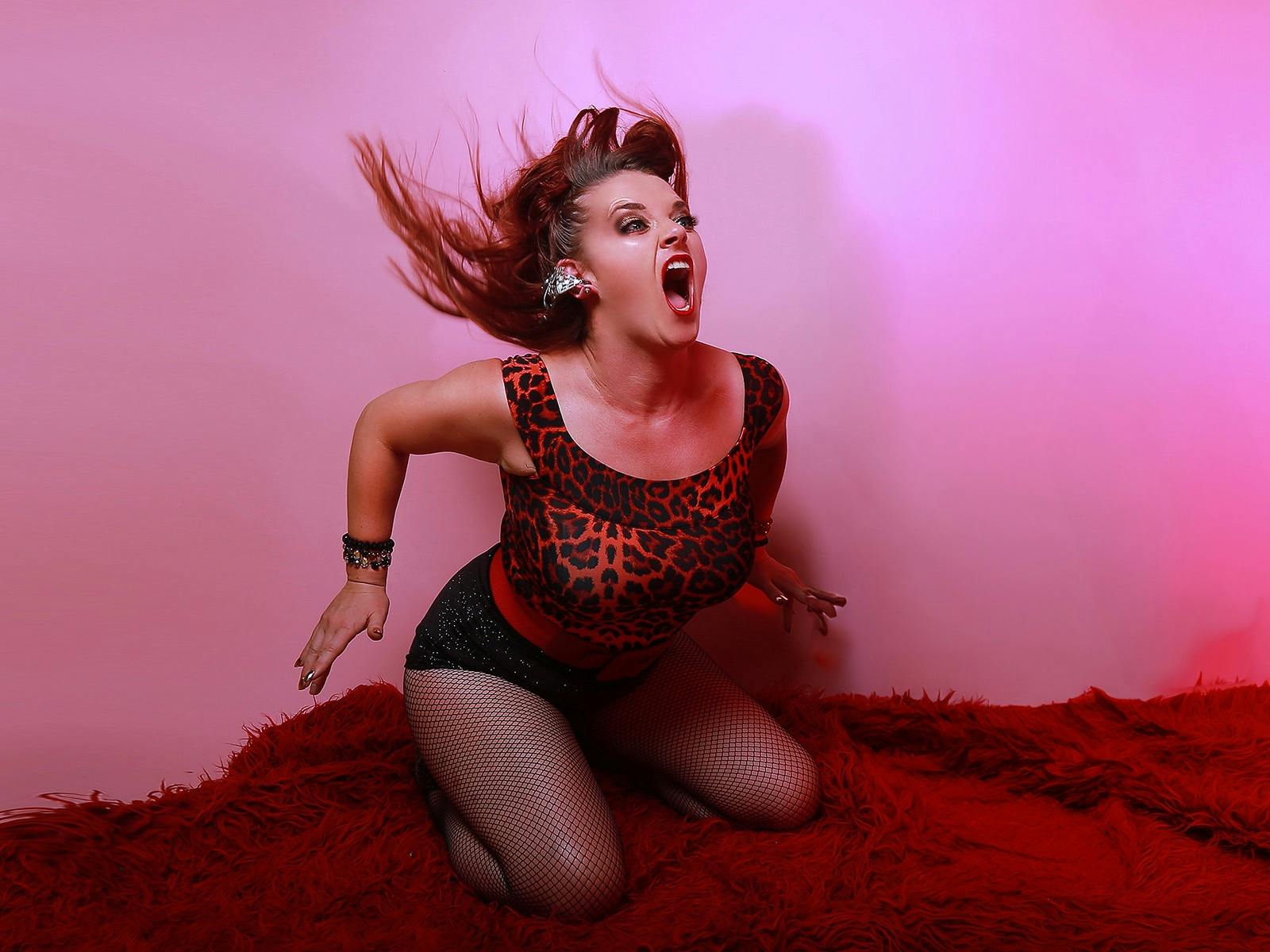 Woman screams with hair flying against a pink wall