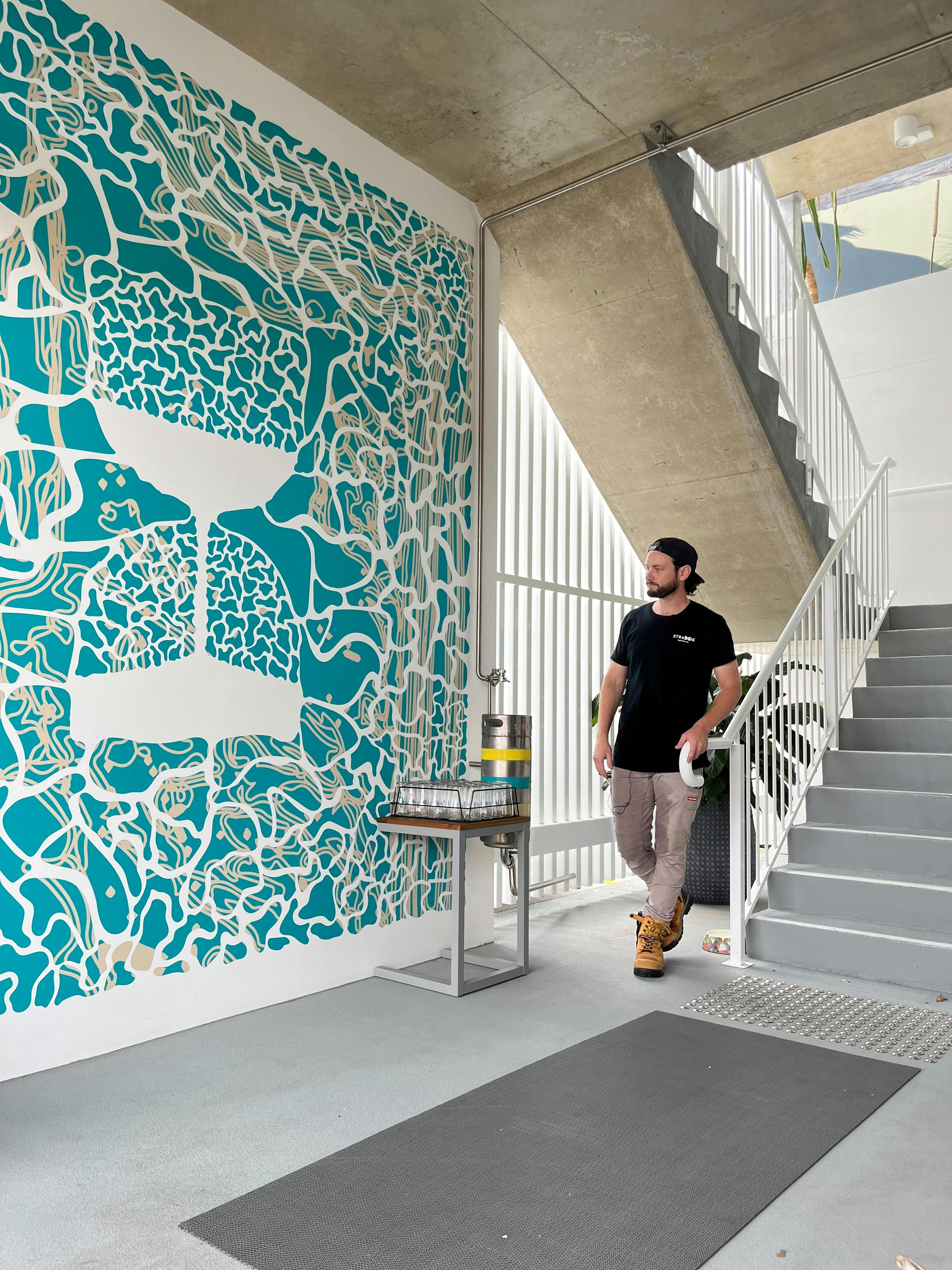 Male Figure stands at the base of stairs, besides a blue mural of an hourglass