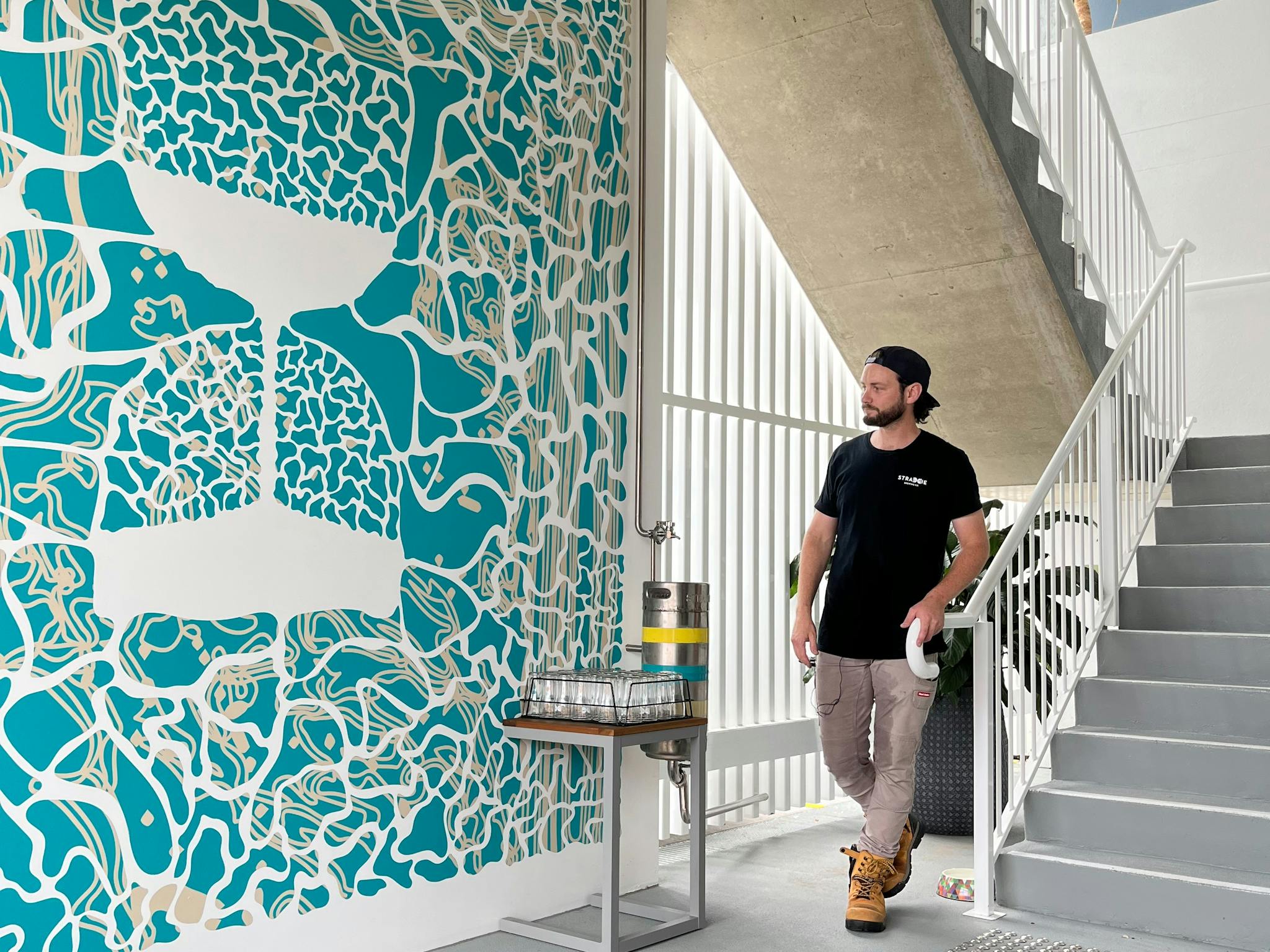 Male Figure stands at the base of stairs, besides a blue mural of an hourglass Male Figure stands at the base of stairs, besides a blue mural of an hourglass