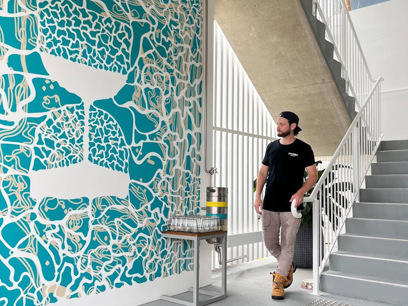 Male Figure stands at the base of stairs, besides a blue mural of an hourglass