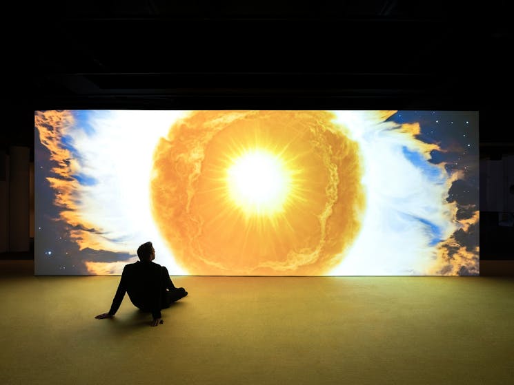 Man sitting on the floor looking at a projection of the Sun's corona