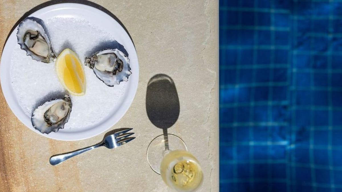 aerial view of three natural oysters and glass of sparkling wine next to a pool.
