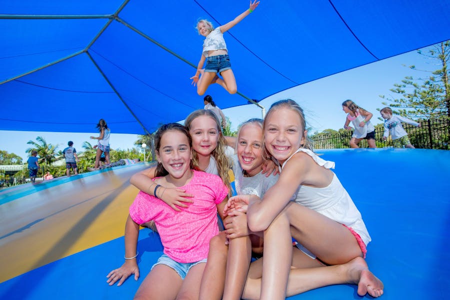 Jumping pillow with a group of friends sitting in the foreground and girl jumping in air behind them