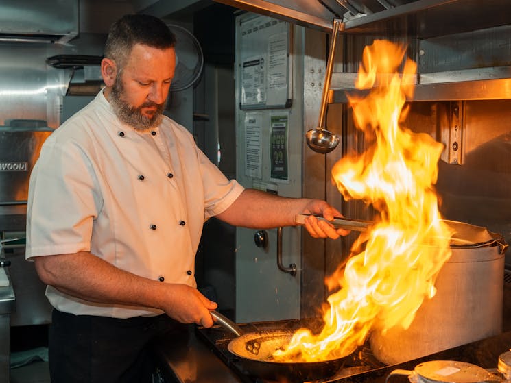 Chef Frank prepares a mouth-watering dish with flames on a gas stove top.