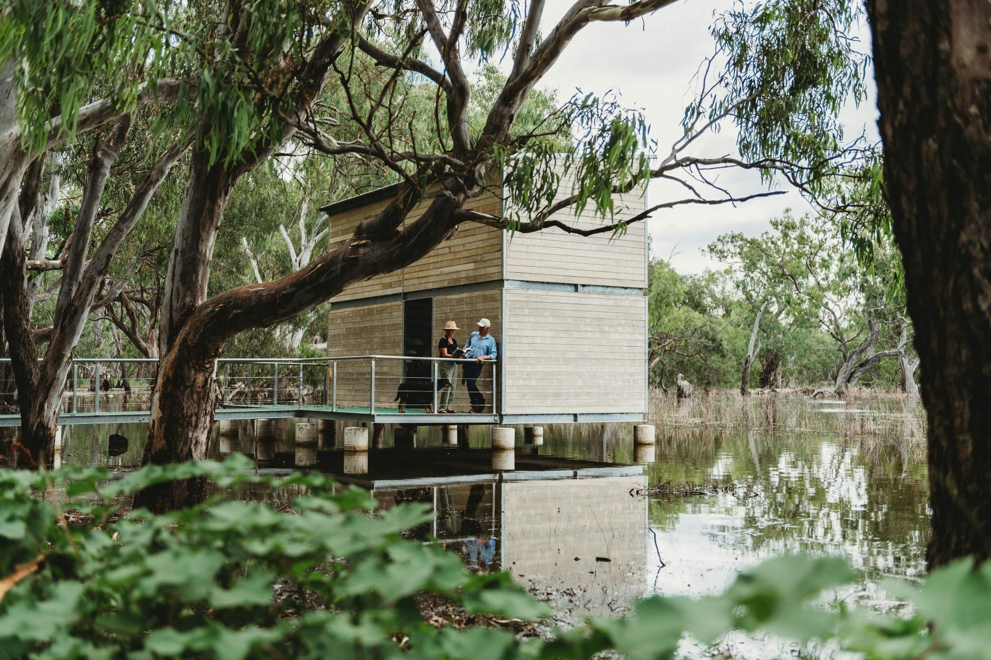 Man and woman stand on bird hide platform overlooking the water