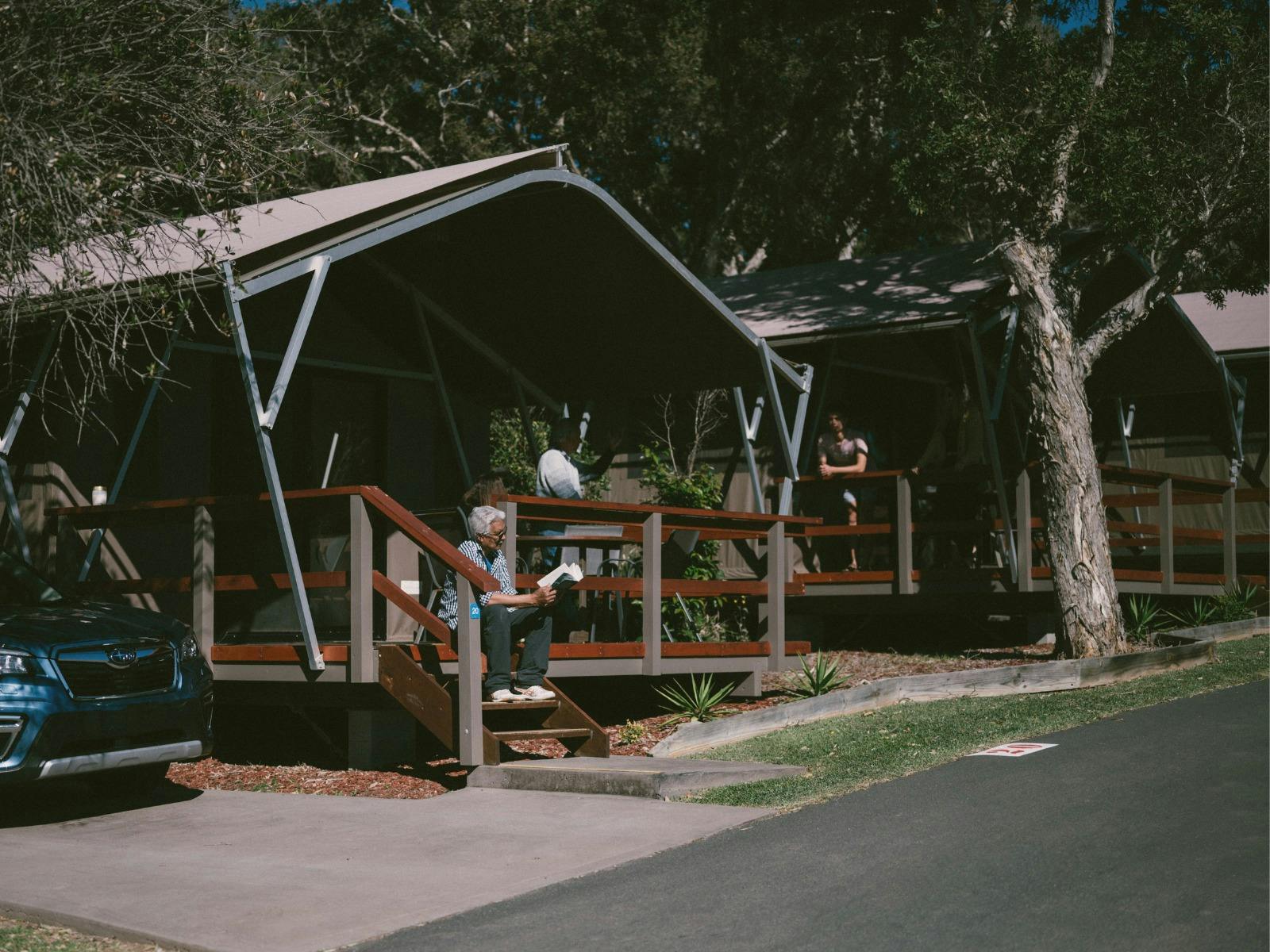Older man sits in front of a beach tent reading.