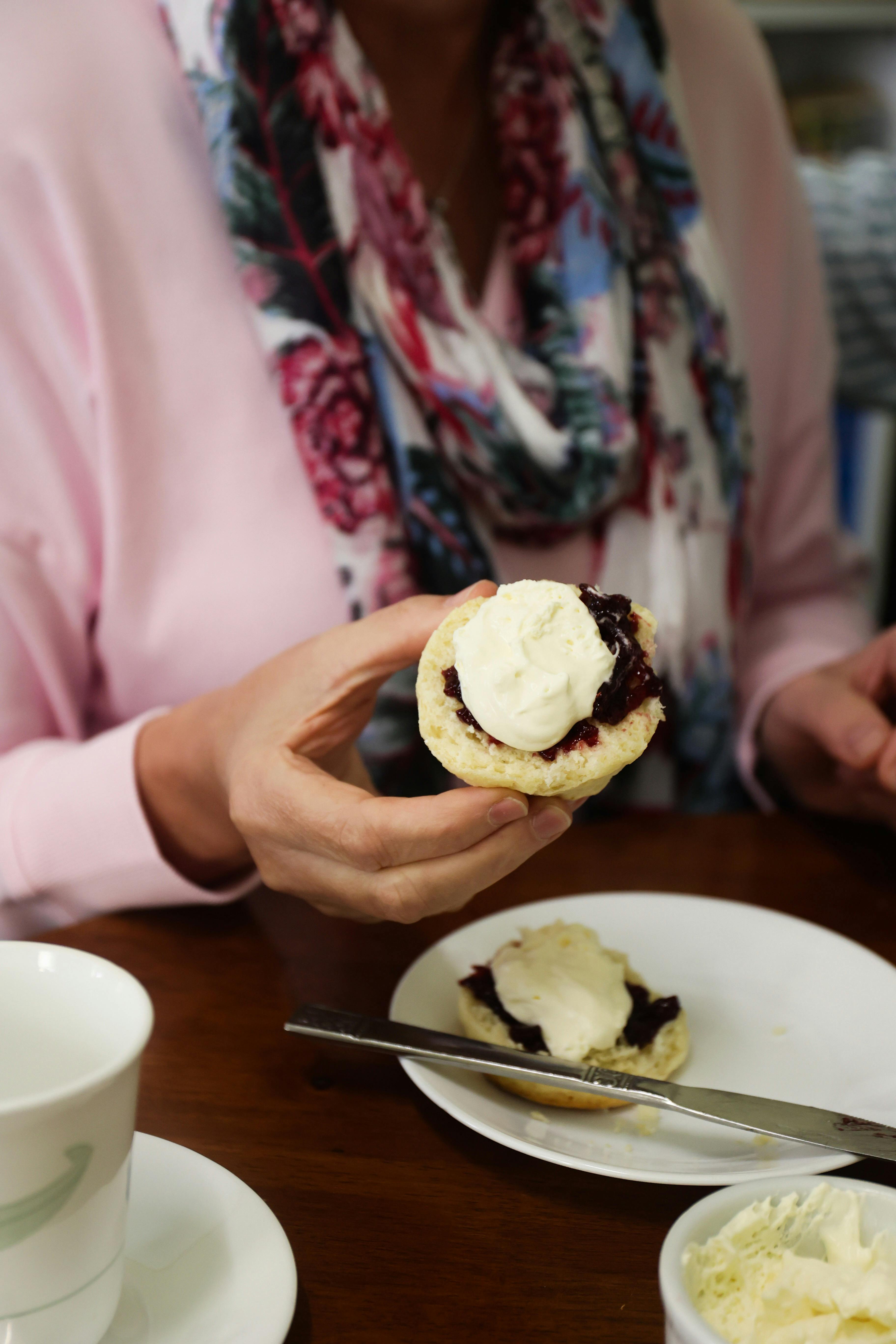 Lady holding up a fresh scone with cream and jam on top.