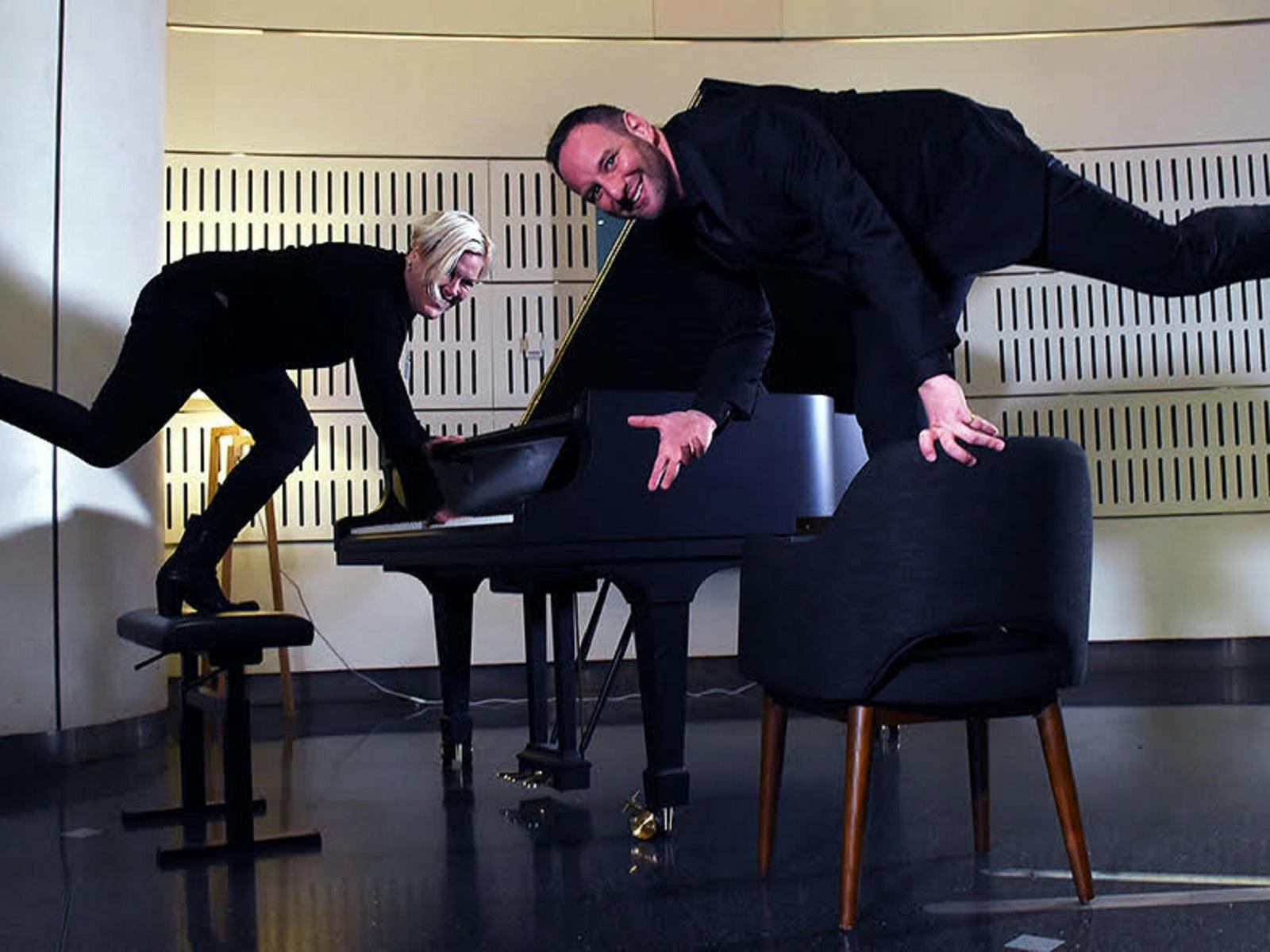 Singer and pianist standing on chairs on one leg