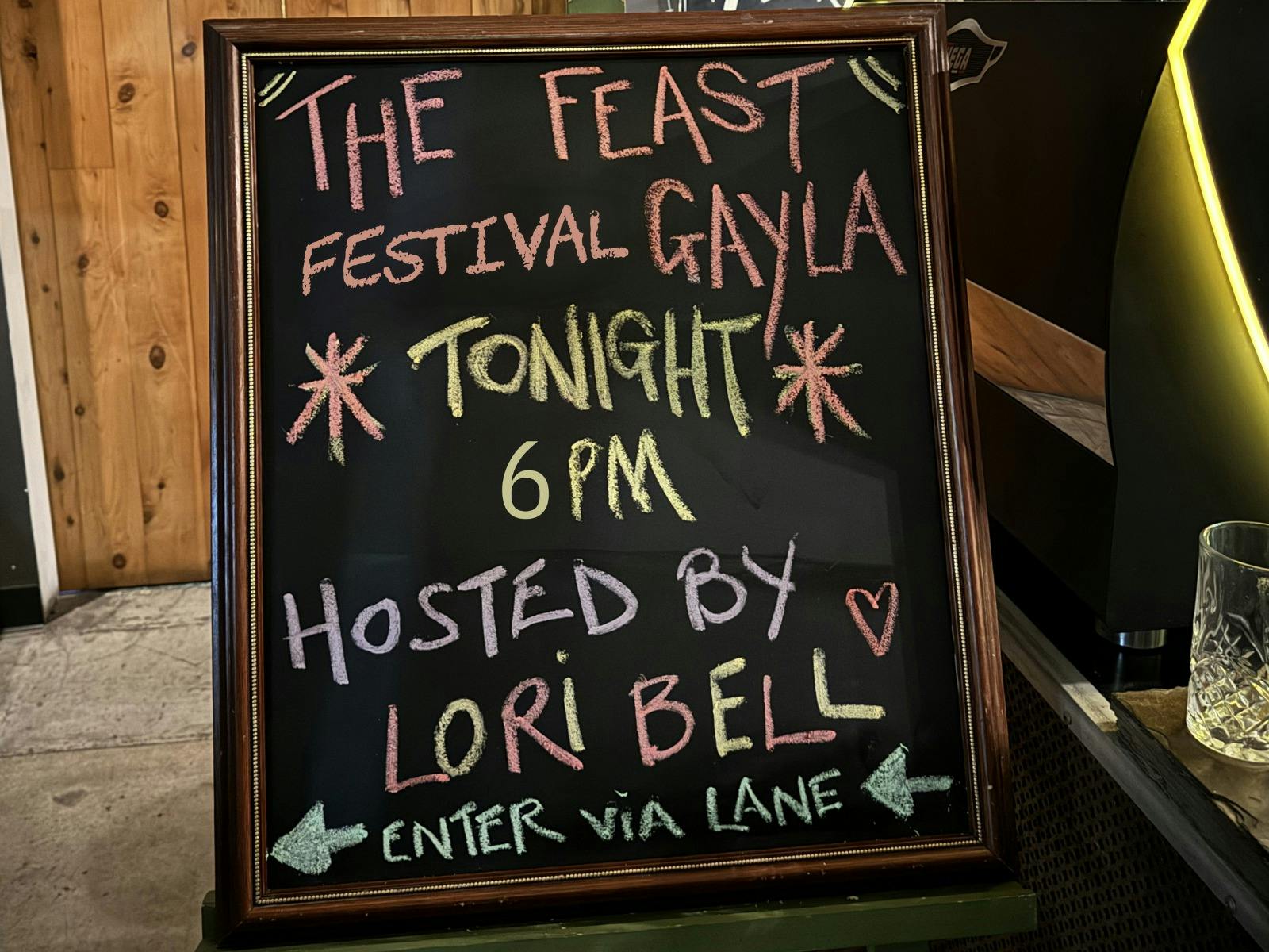A blackboard with 'The Feast Festival Gayla tonight 6pm hosted by Lori Bell' written in  chalk.