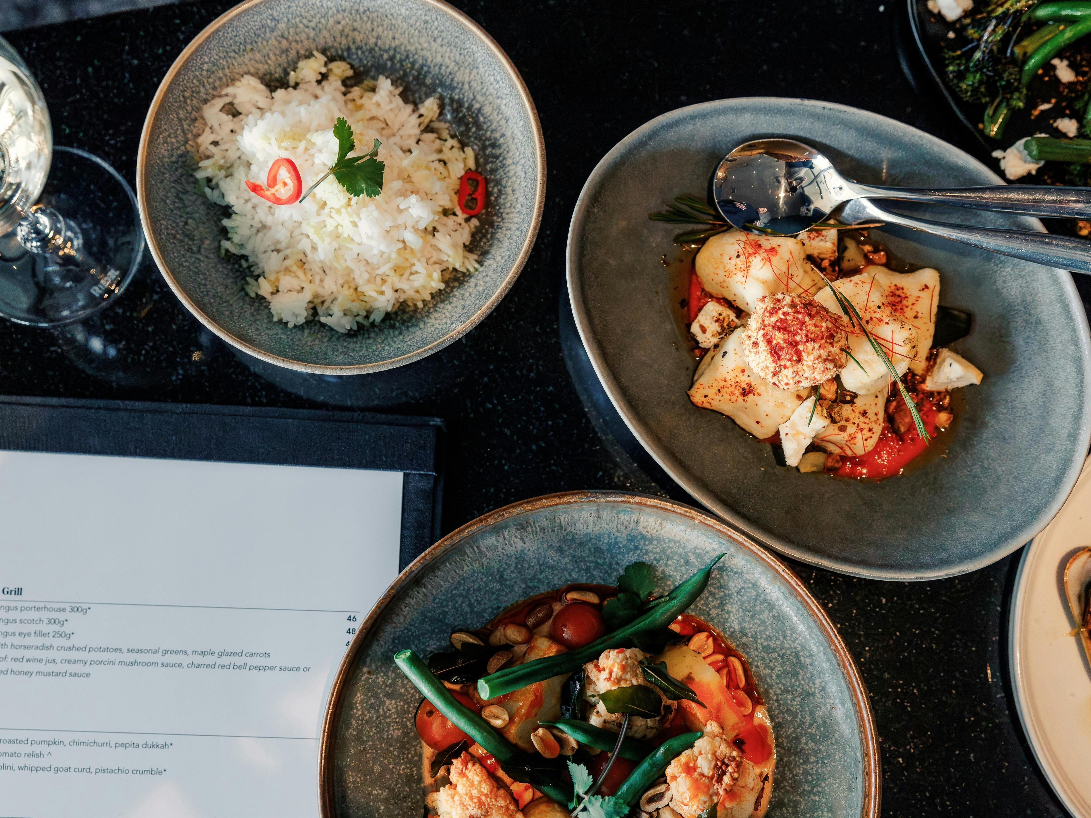 Three main course dining dishes at warmly presented dining table with a glass of wine and menu