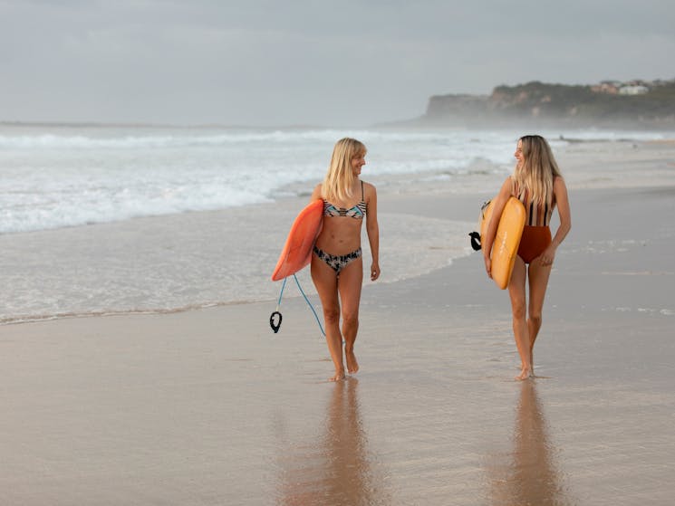 women walking at the beach with surfboards
