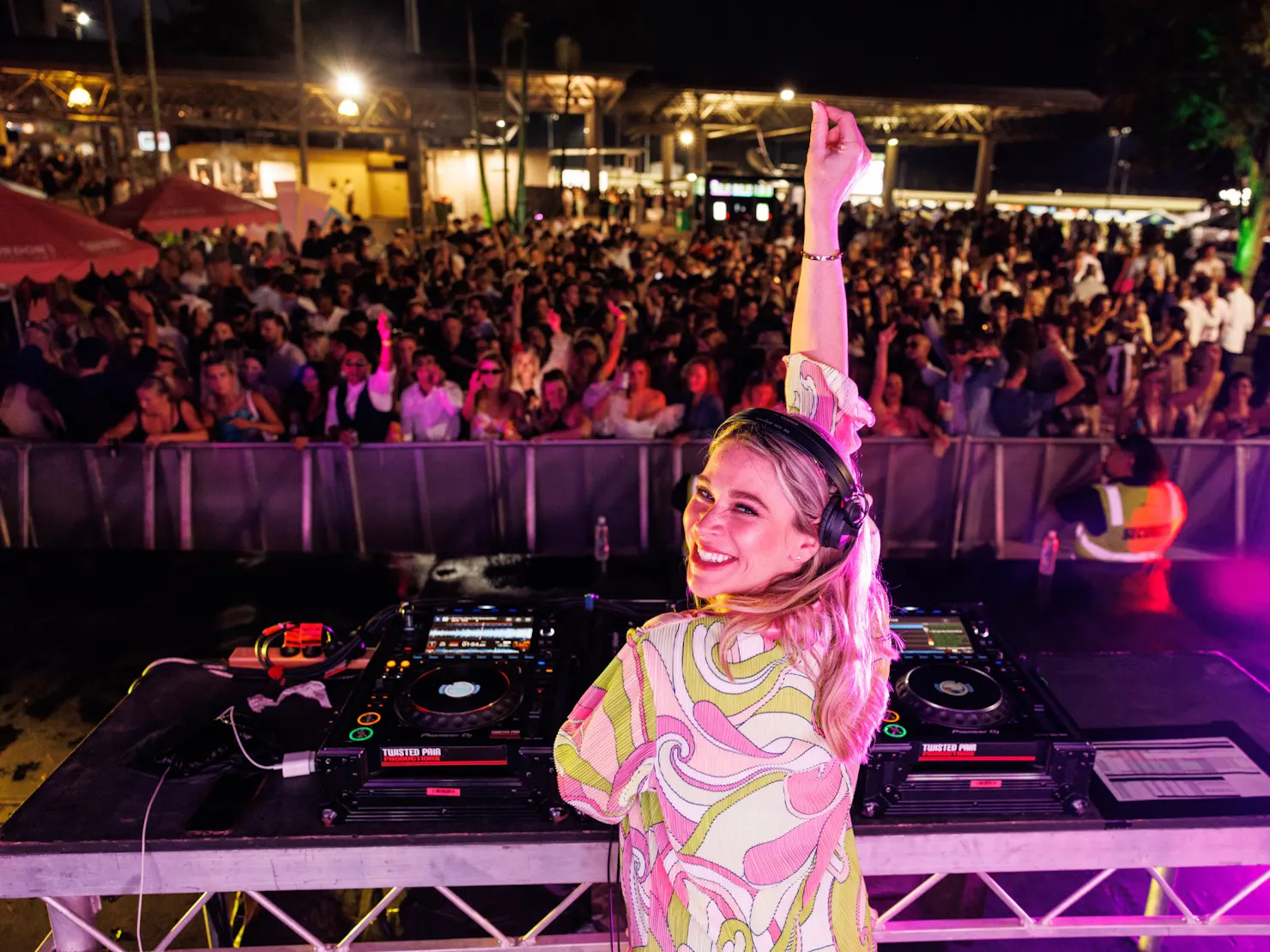 Female DJ playing to a crowd of people in the background