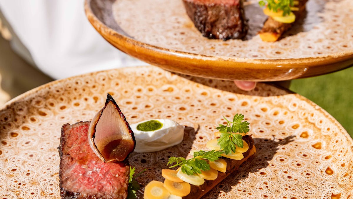 Photo of chef carrying two food dishes featuring steak and sides
