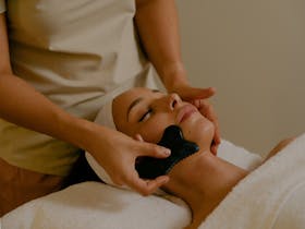 A therapist massaging the guest’s face with a guasha stone
