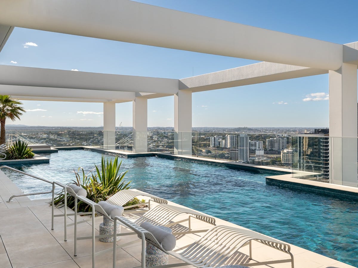 Outdoor rooftop swimming pool with white lounge chairs and plants surrounding.