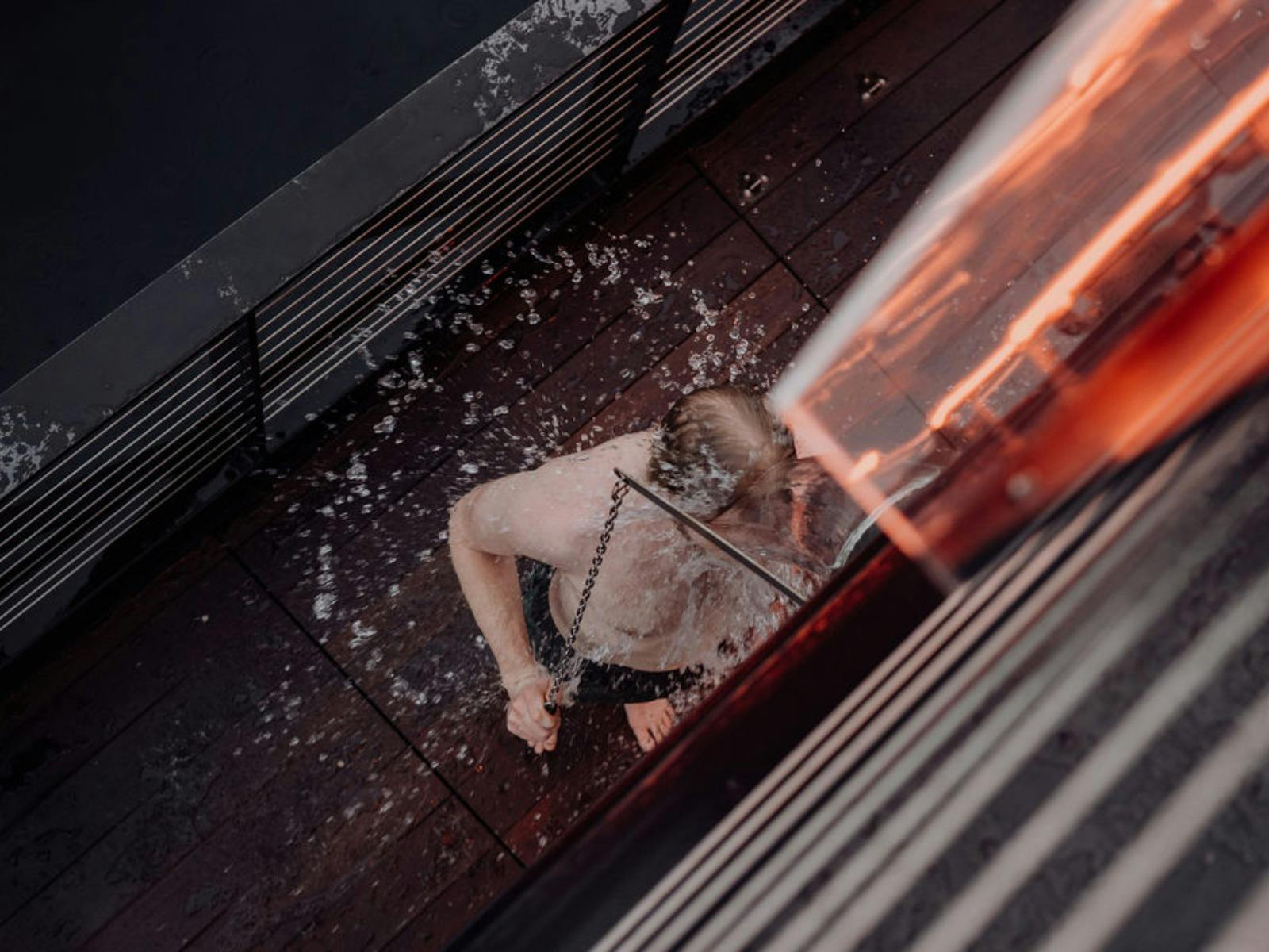 High-angle shot of a person rinsing under a cold bucket shower on a wooden deck.