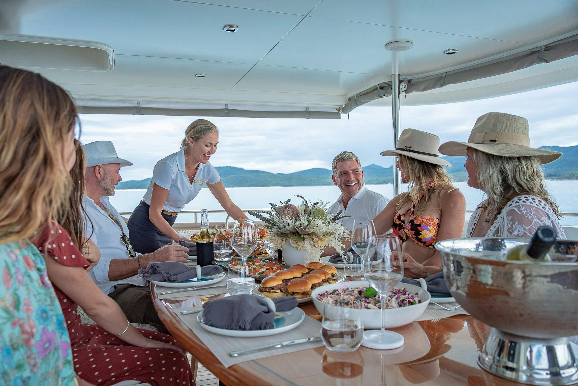 Chief Stewardess of Texas T serves group of guests food on rear deck of Texas T motor yacht
