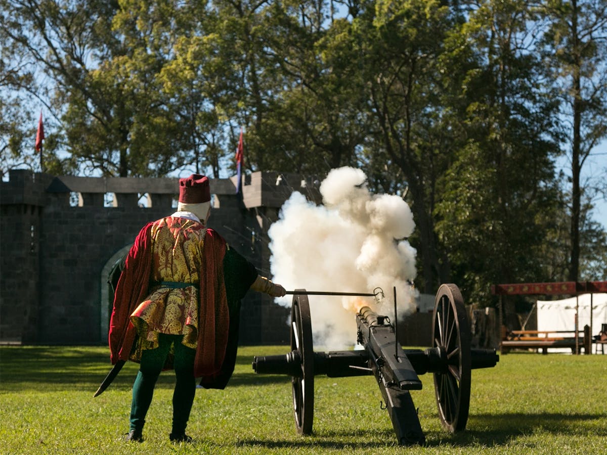 A cannon fires towards the castle as a plume of smoke and sparks of flame erupts from the barrel.