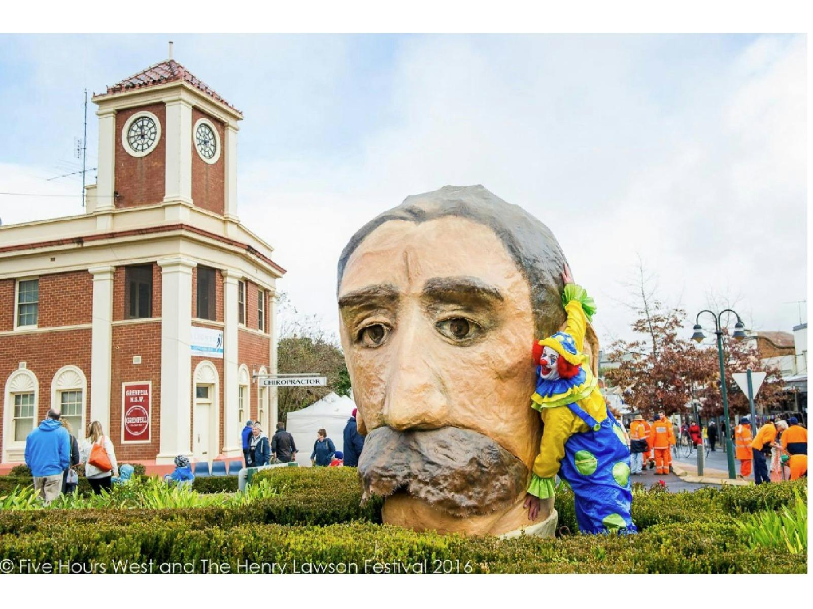 A photo of a paper mache Henry Lawson head with a clown hugging it