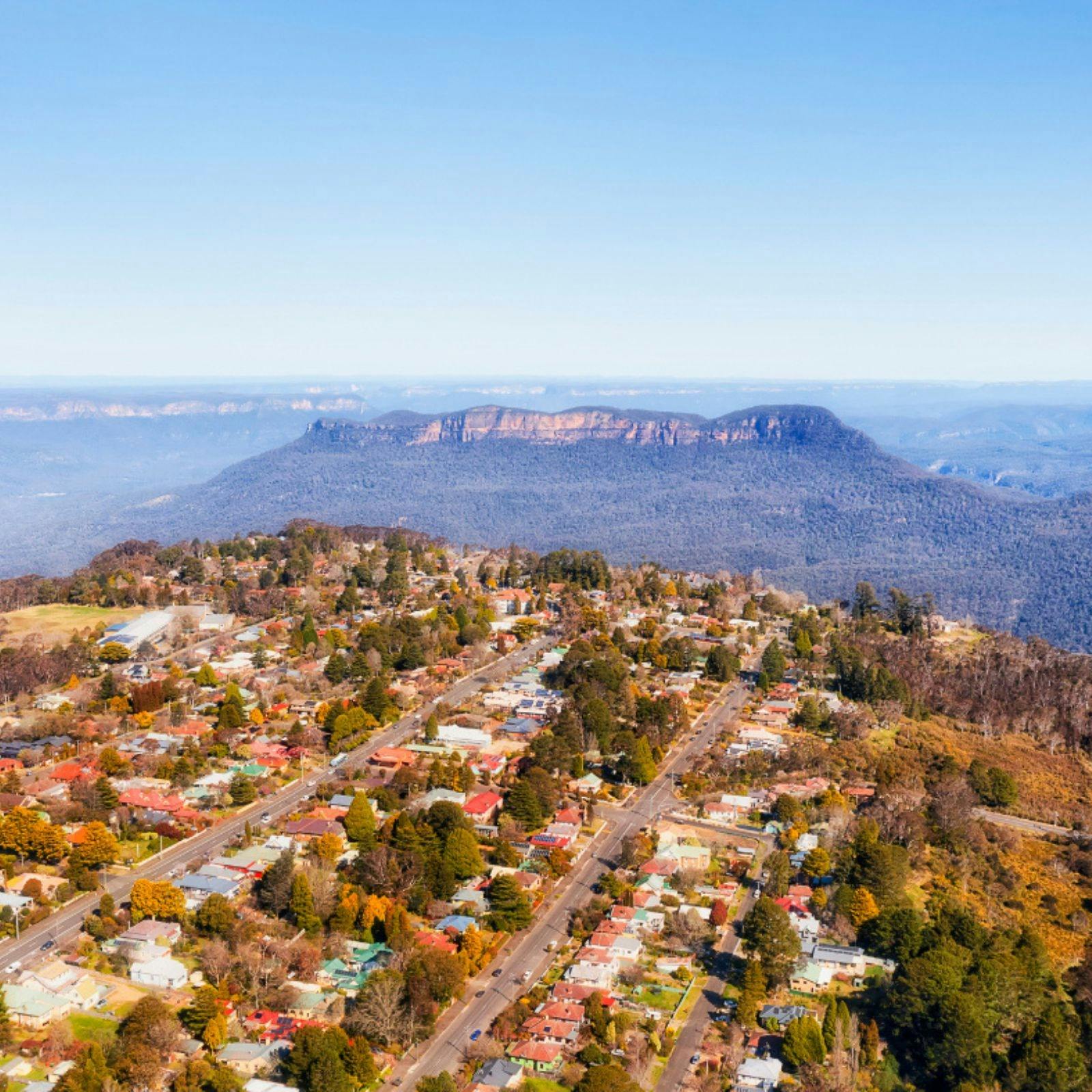An aerial view of a town in the foreground and the Blue Mountains in the background